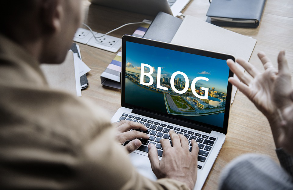 a man is typing on a laptop with the word blog on the screen