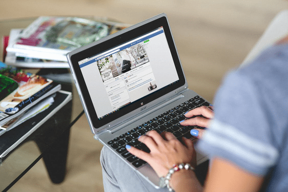 a woman is typing on a laptop with a facebook page open