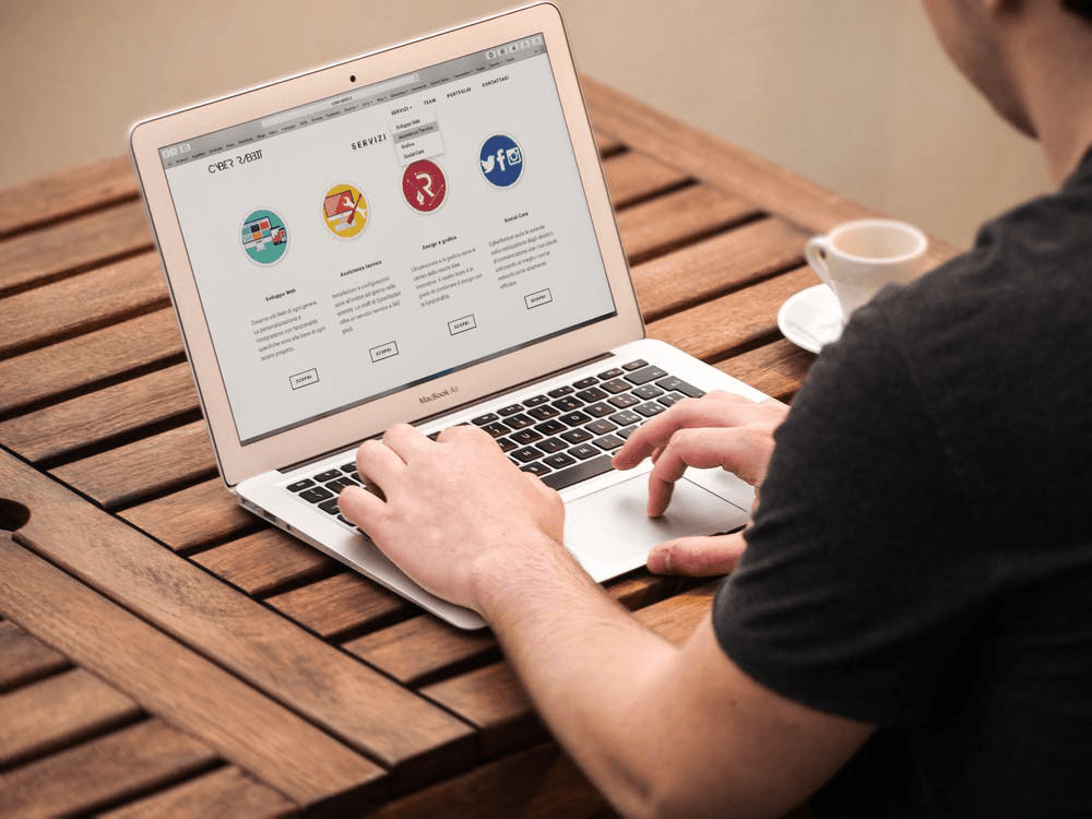 a man is typing on a macbook air on a wooden table