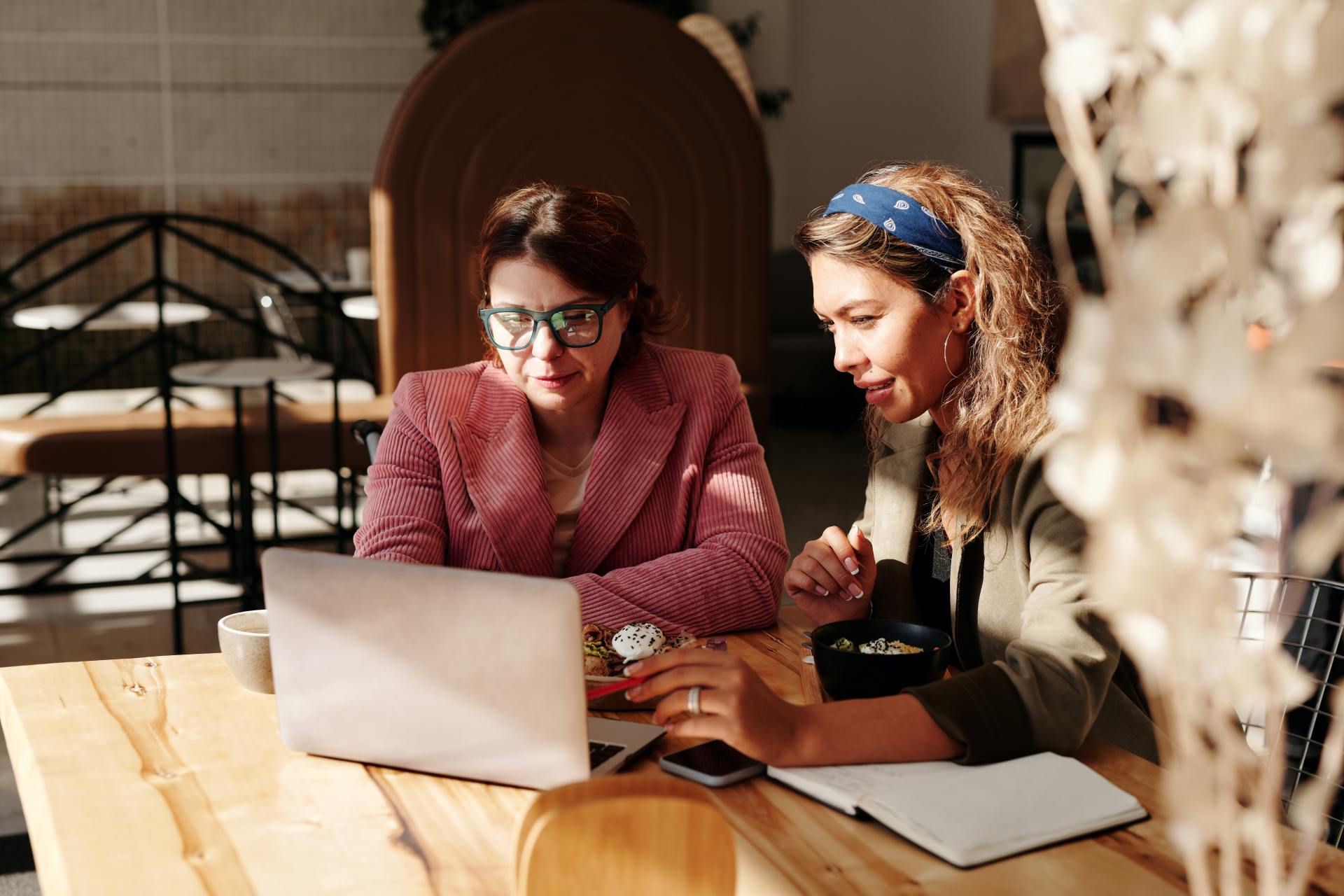 two women are sitting at a table looking at a laptop .