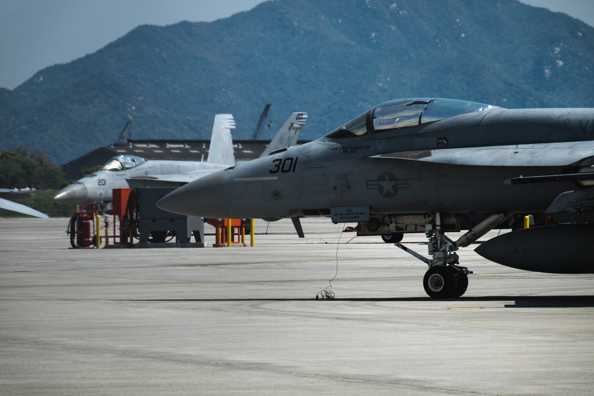 A row of fighter jets are parked on a runway with mountains in the background.