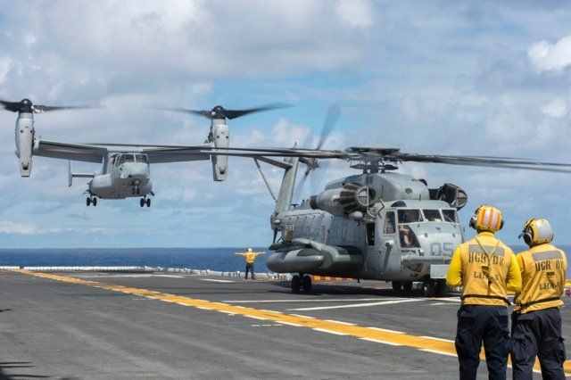 A couple of men standing next to a helicopter on a runway.