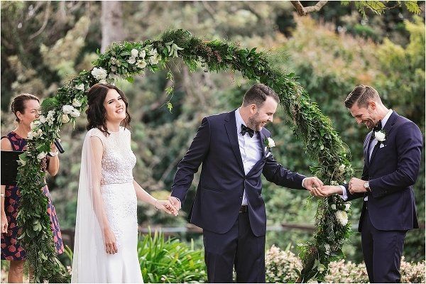 bestman passing rings to groom at an elegant Spicers Clovelly hinterland wedding, bride in white waits under arbor
