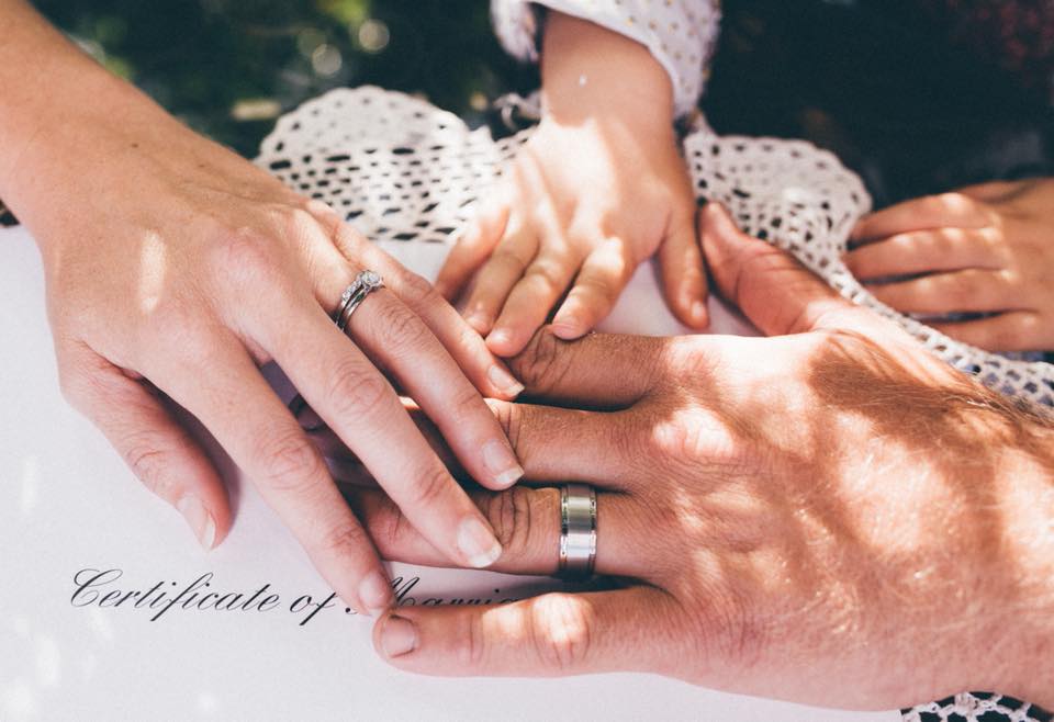 bride and grooms hand with new wedidng rings and their little child's hand with them on marriage certificate envelope