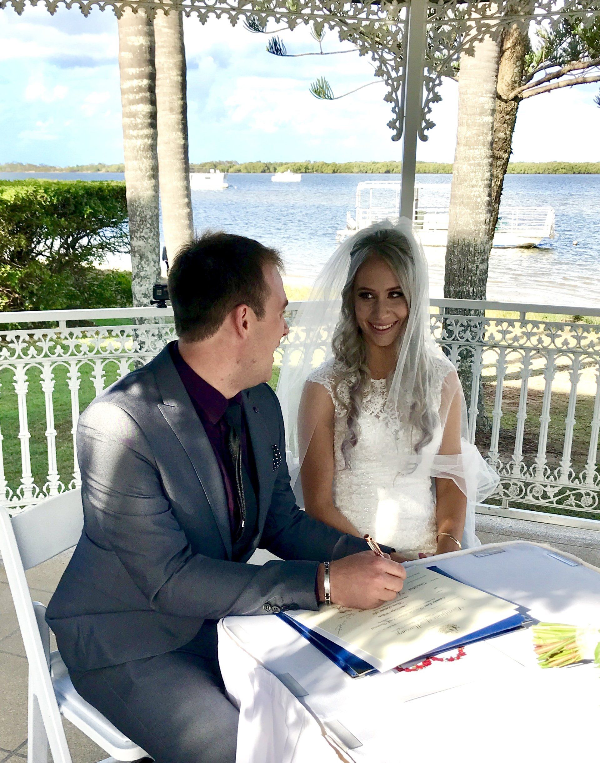 bride with veil at wedding gazebo at Caloundra Powerboat Club wedding, groom in grey shiny suit signing