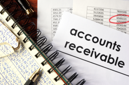 Accounts receivable paperwork on a desk with calculator, notebook, and highlighted ledger entries