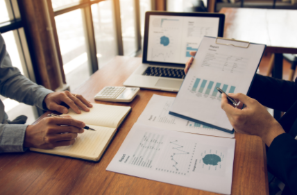 Hands reviewing financial charts and graphs at a desk with laptop and notebook