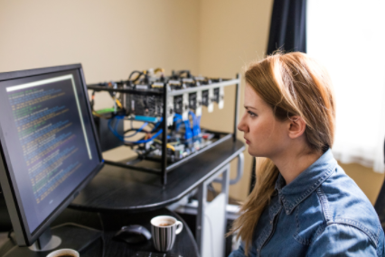 Person at a desk looking at code on a monitor beside a small 3D printer setup