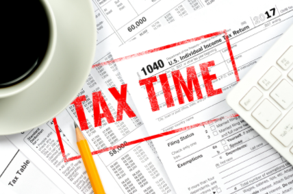 Tax forms with bold red “TAX TIME” stamp, coffee cup, pencil, and calculator on a desk