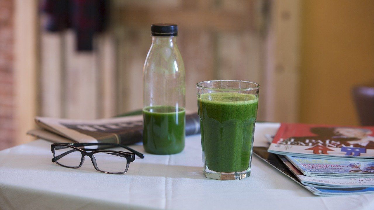 Une bouteille de jus vert et un verre de jus vert sont sur une table.