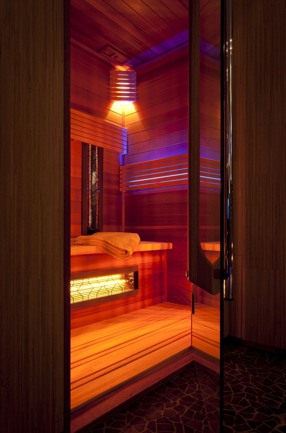 Un sauna en bois avec une porte vitrée et des lumières violettes.