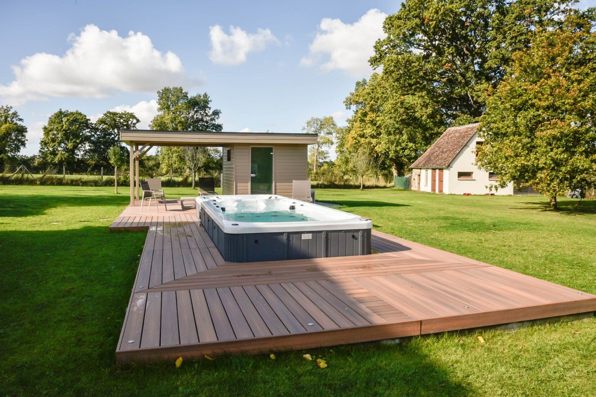 Un bain à remous est installé sur une terrasse en bois au milieu d'un champ verdoyant.