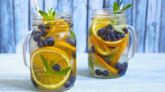 Deux pots Mason remplis d'eau, de tranches de citron, de myrtilles et de feuilles de menthe.