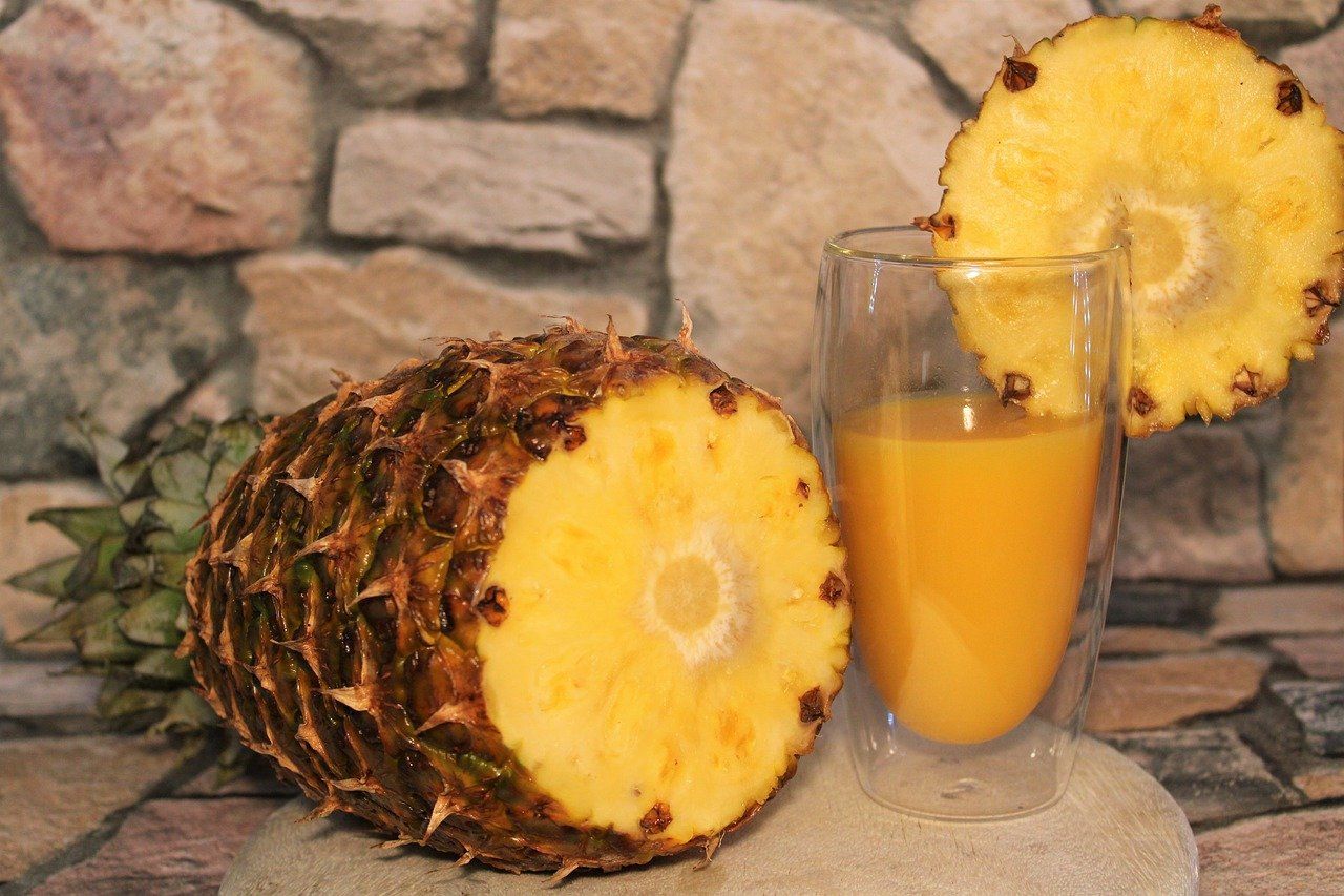 Un ananas assis à côté d'un verre de jus d'ananas.