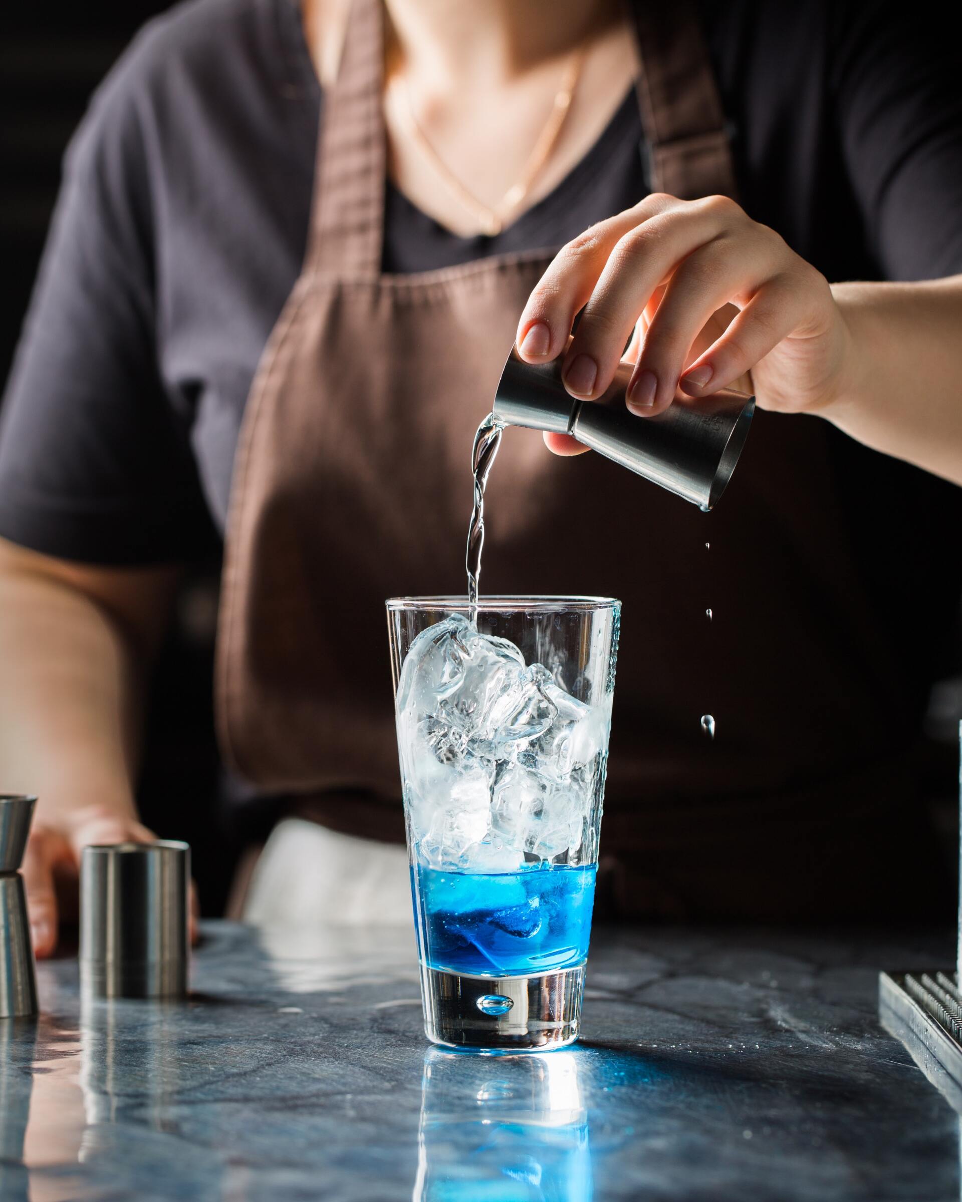Un camarero está sirviendo una bebida azul en un vaso con hielo.
