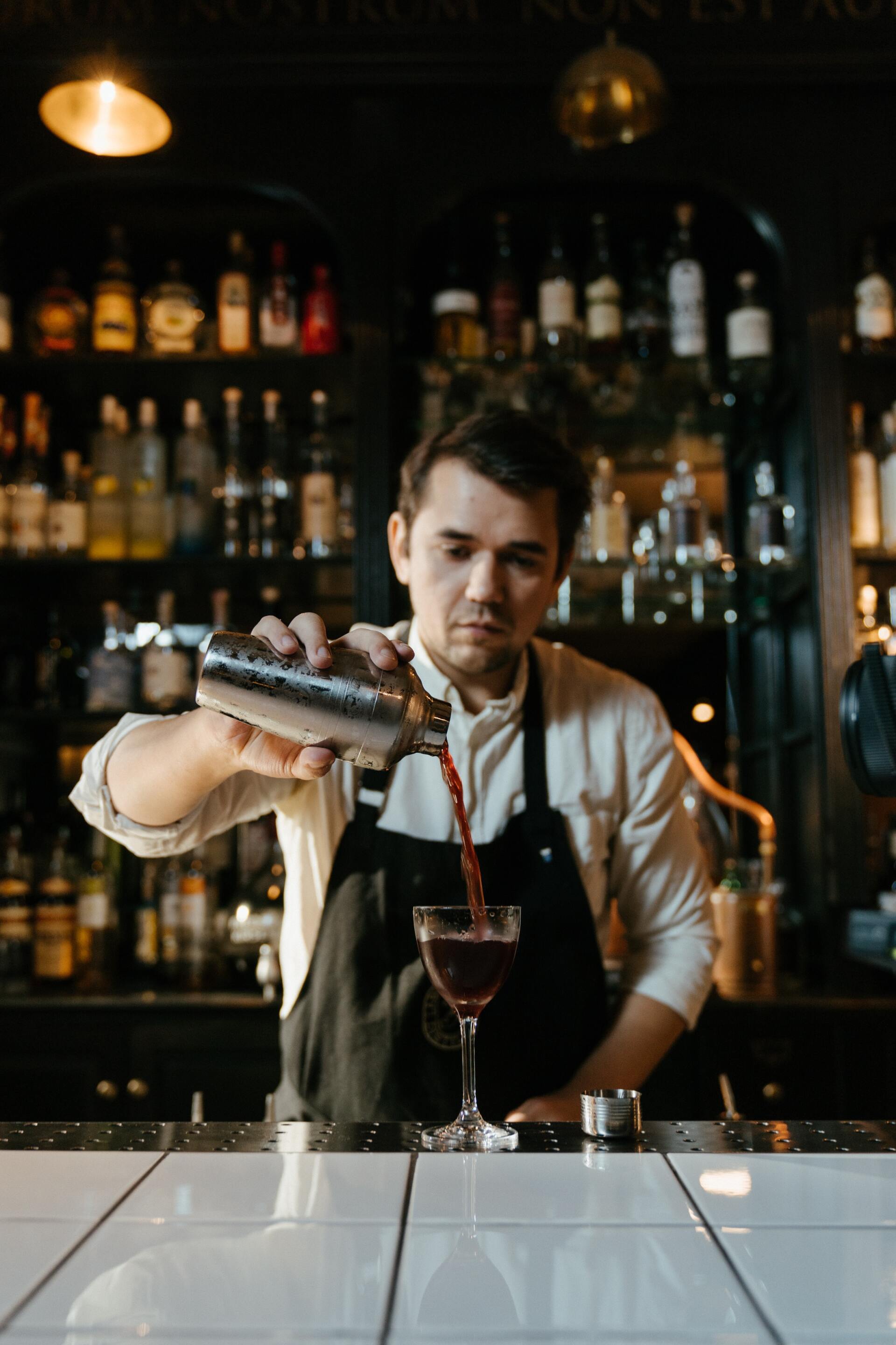 Un camarero está sirviendo una bebida en un vaso en un bar.