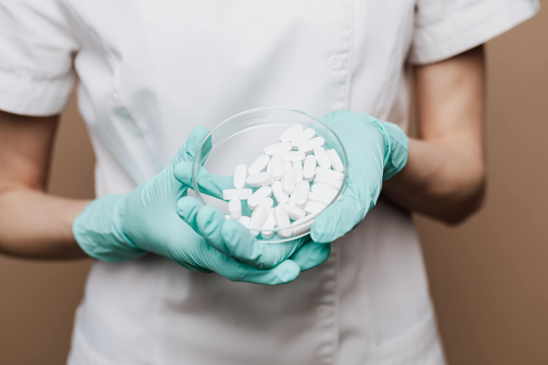 Una enfermera con guantes sostiene una placa de Petri llena de pastillas.