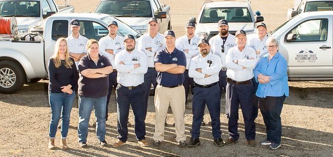 Group of people standing in front of parked trucks in a dusty outdoor lot