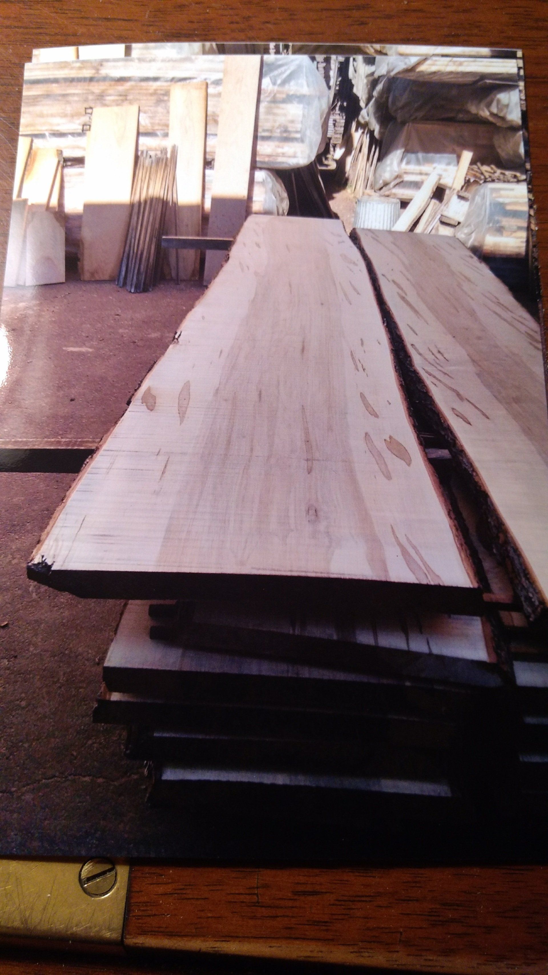 Stack of light-colored, unfinished wood planks in a workshop; other wood visible in the background.