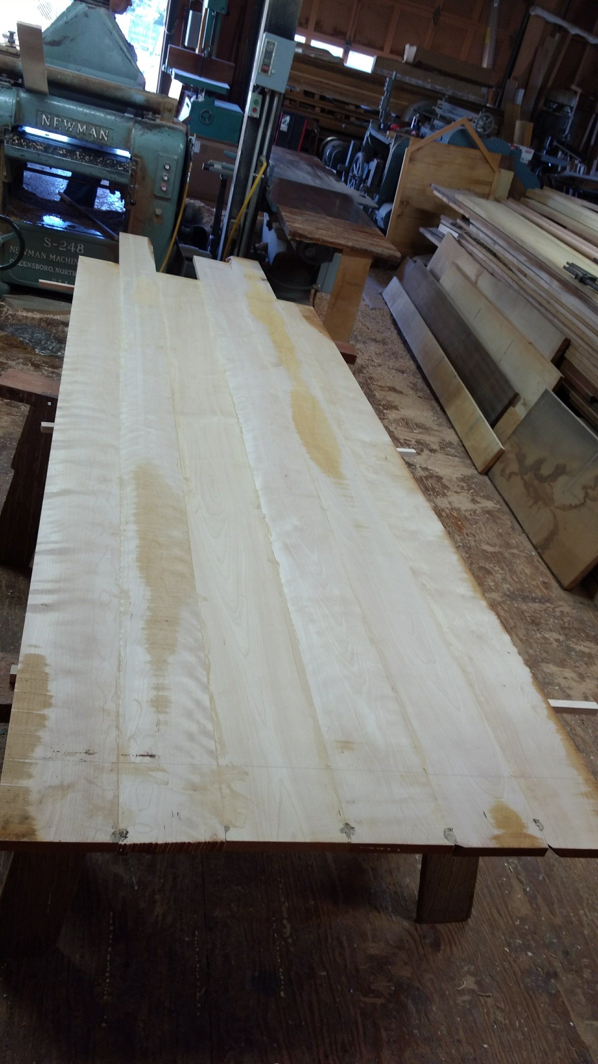 Light-colored wood planks laid on a wooden table in a woodworking shop.
