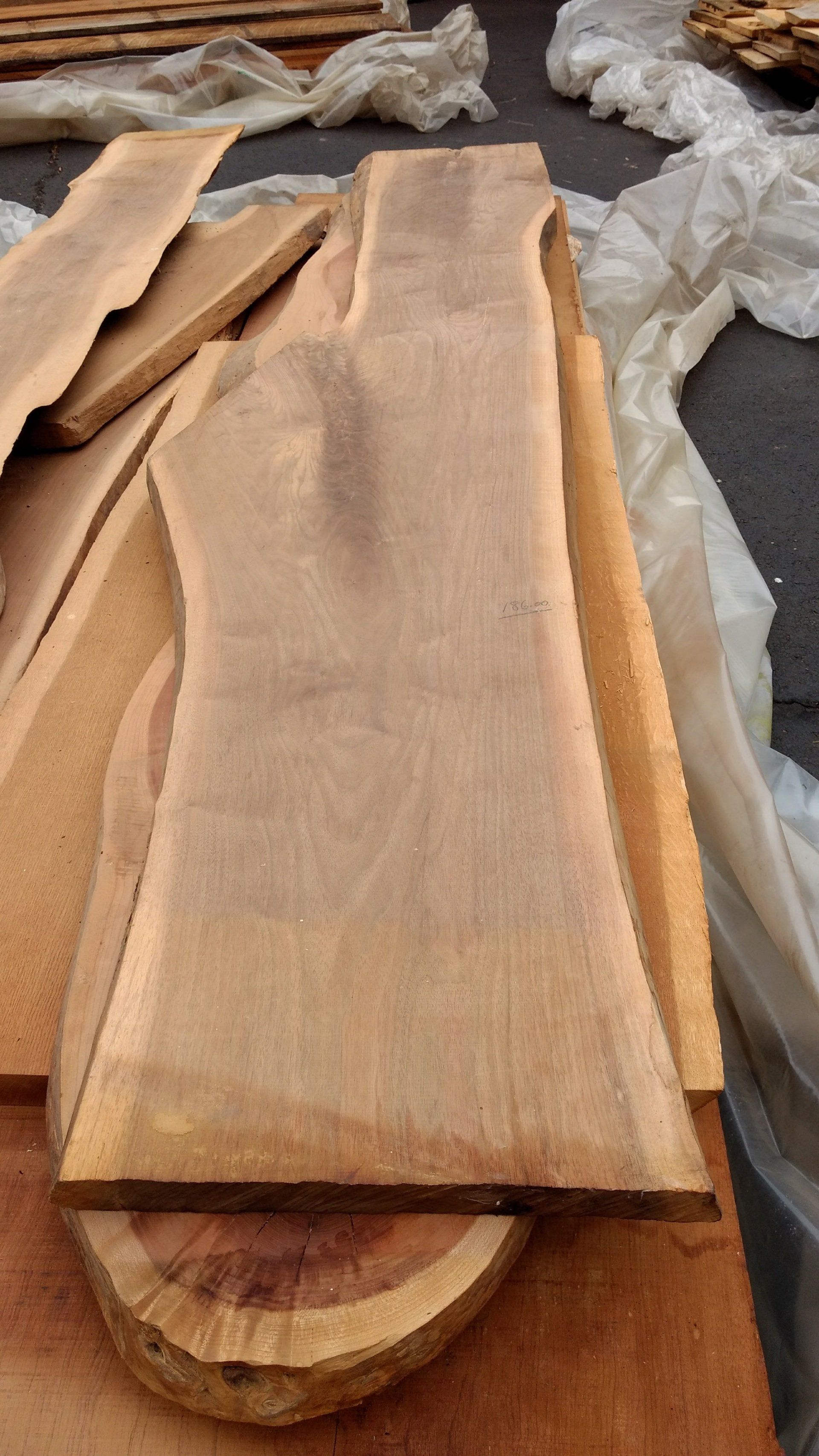 Wooden planks stacked, showing natural wood grain and shape, outdoors.