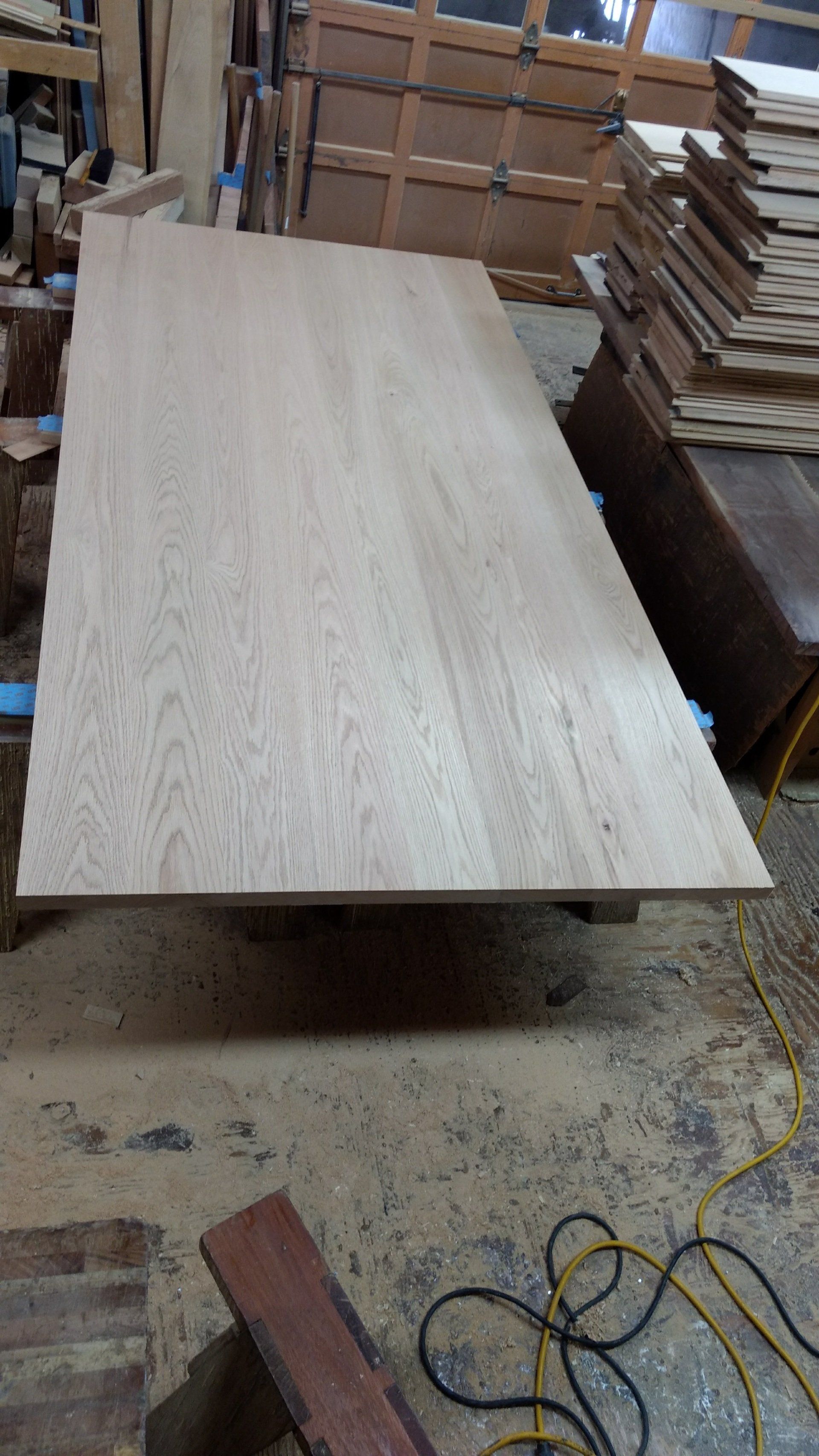 Large, unfinished wood tabletop on a workbench in a workshop.