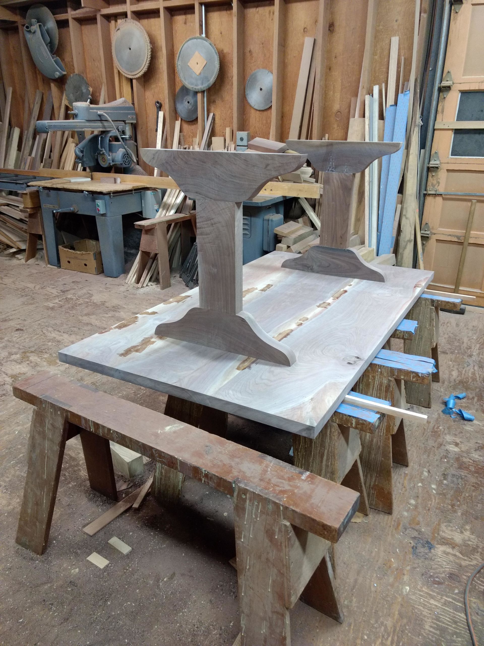 Metal table legs supporting a large gray tabletop in a workshop. Sawhorses and tools are visible in the background.