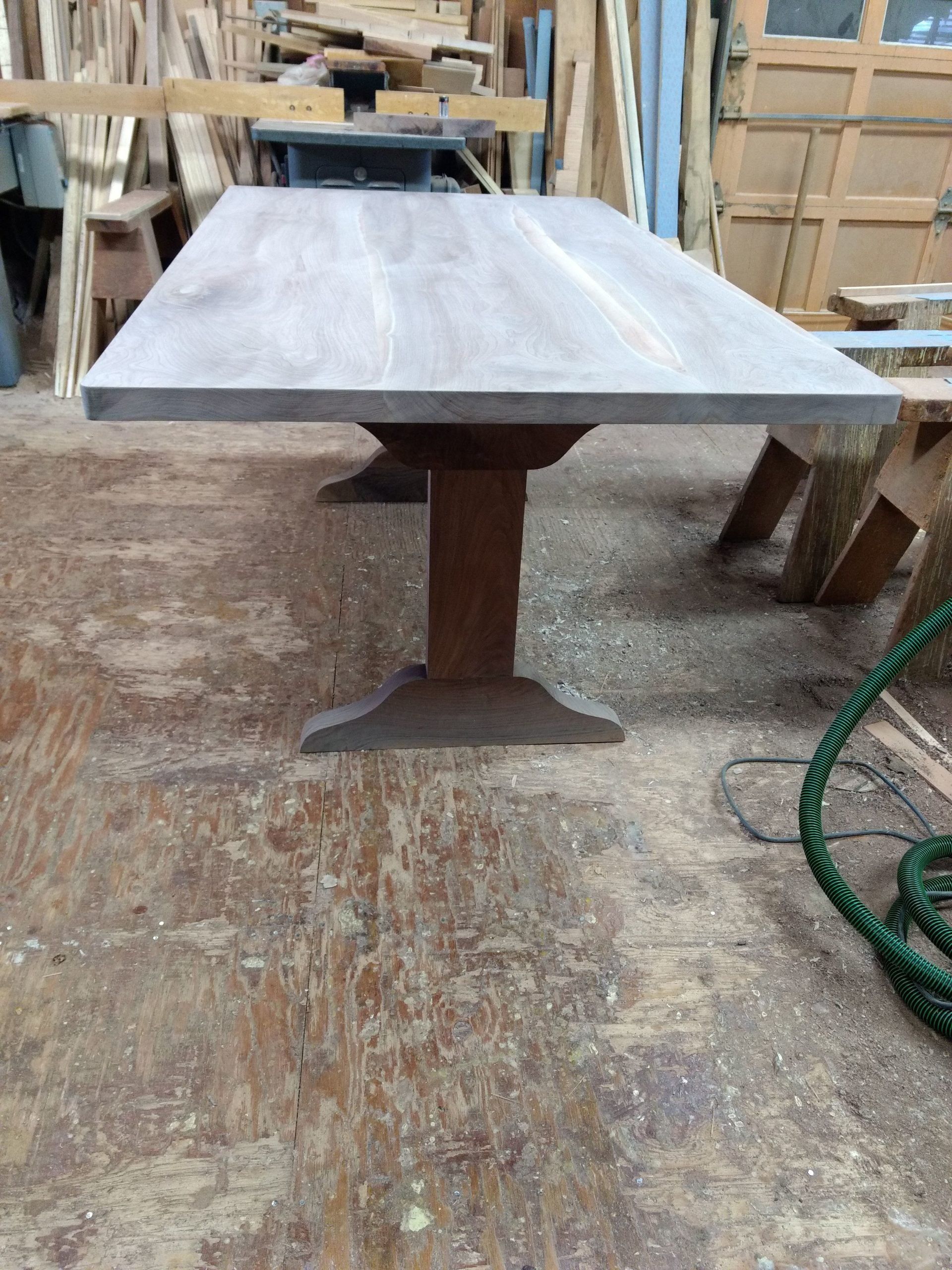 Wooden dining table with a dark base and a light top, in a woodworking shop.