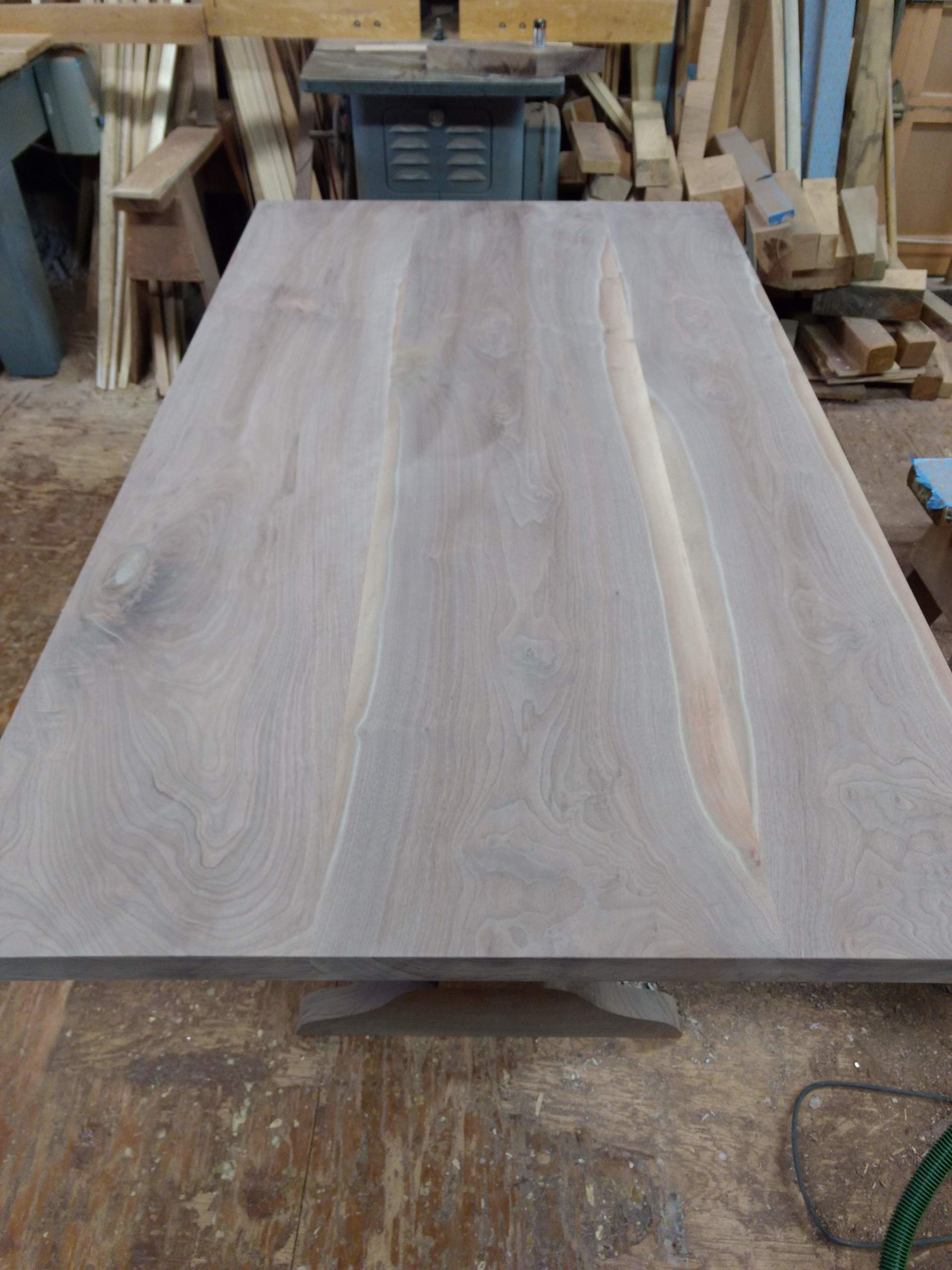 Large, light-toned wooden table on a workbench, likely in a workshop.