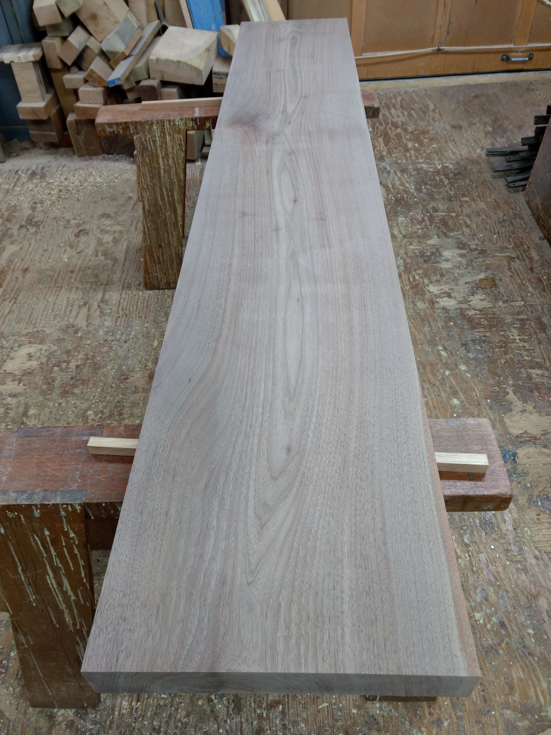 Long, light-brown wood plank on a workbench in a workshop.