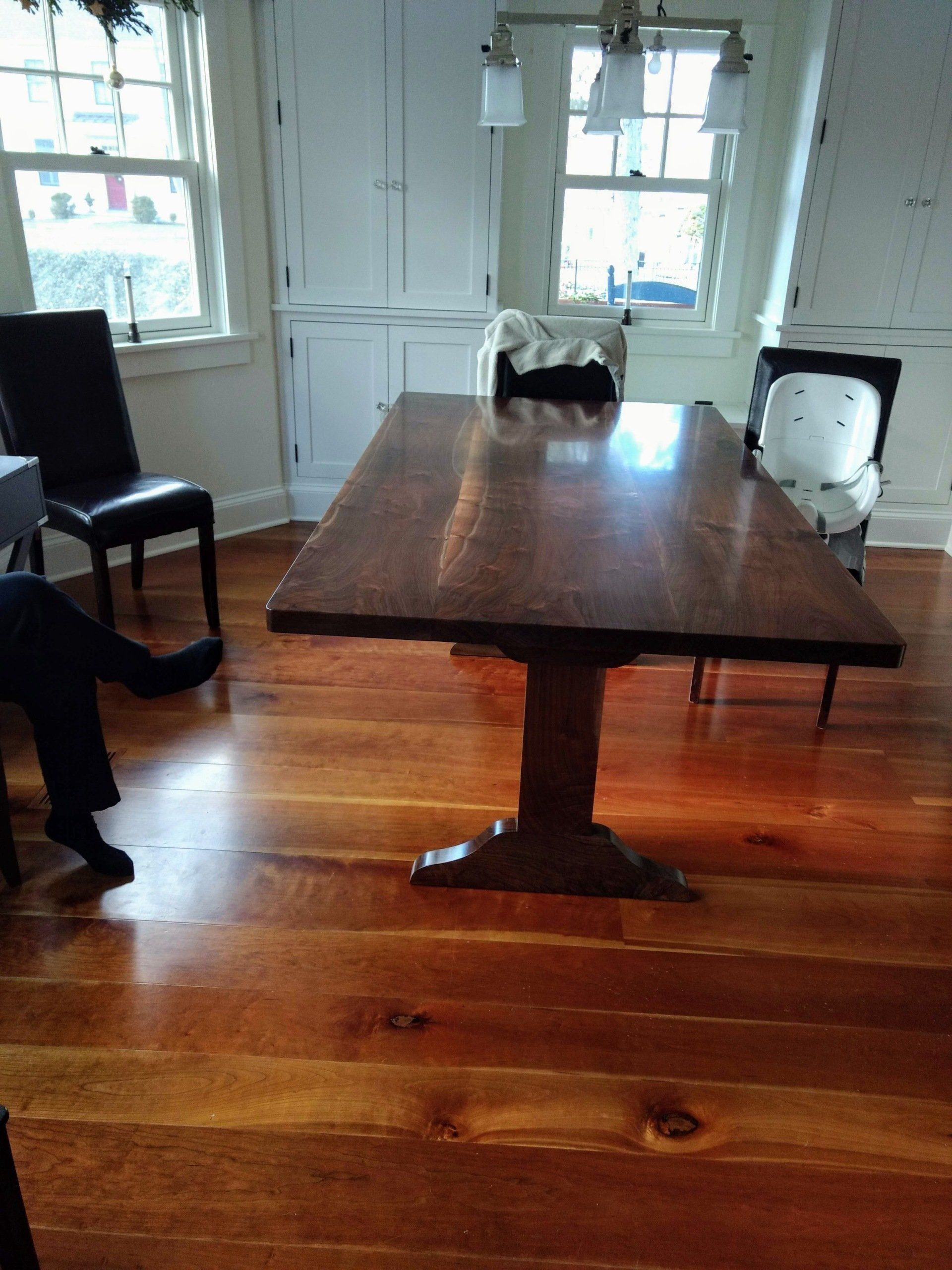 A wooden dining table in a room with hardwood floors, flanked by chairs near windows.