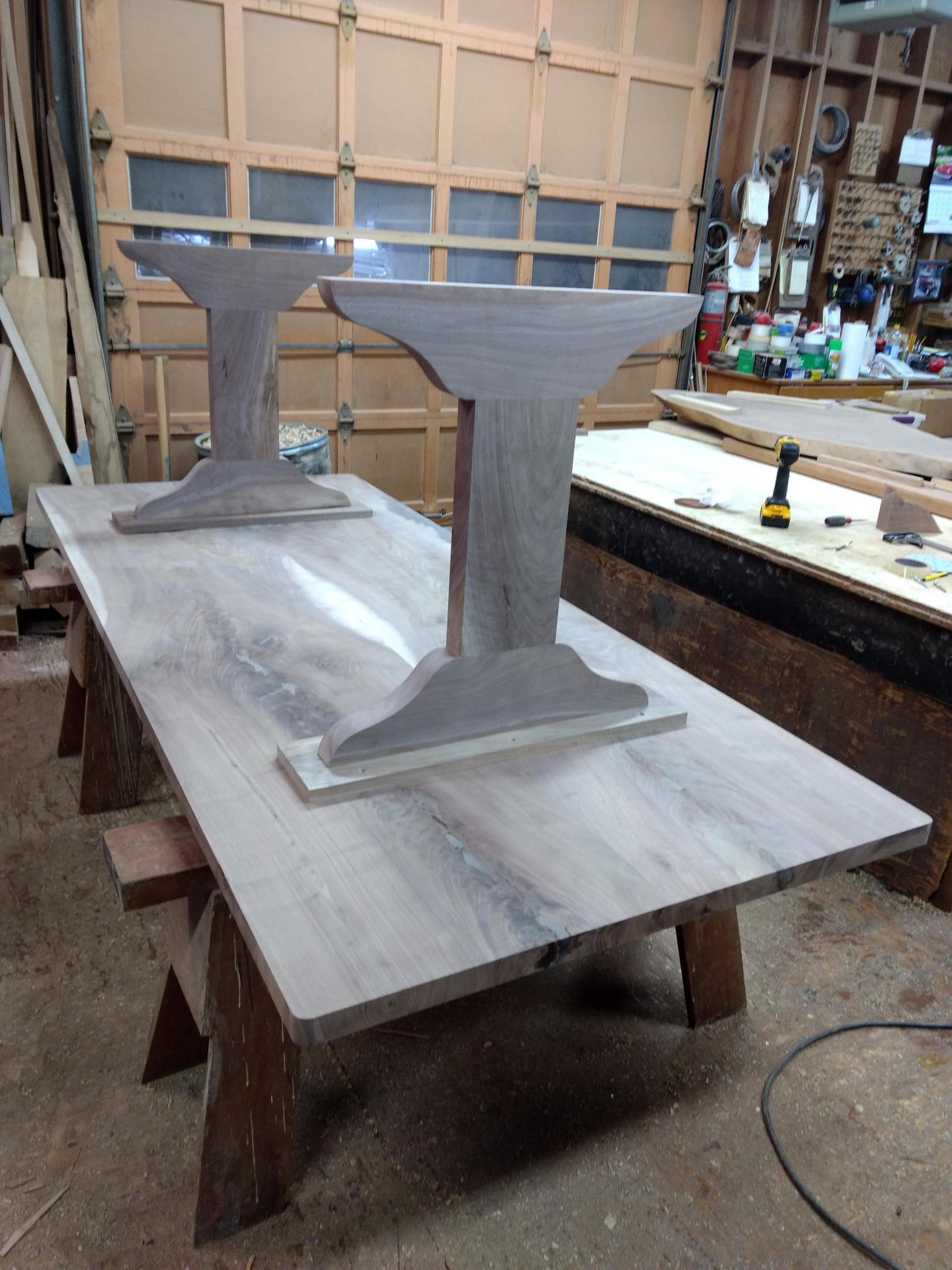 Two-pedestal wooden table in a workshop, unfinished top, legs mounted.