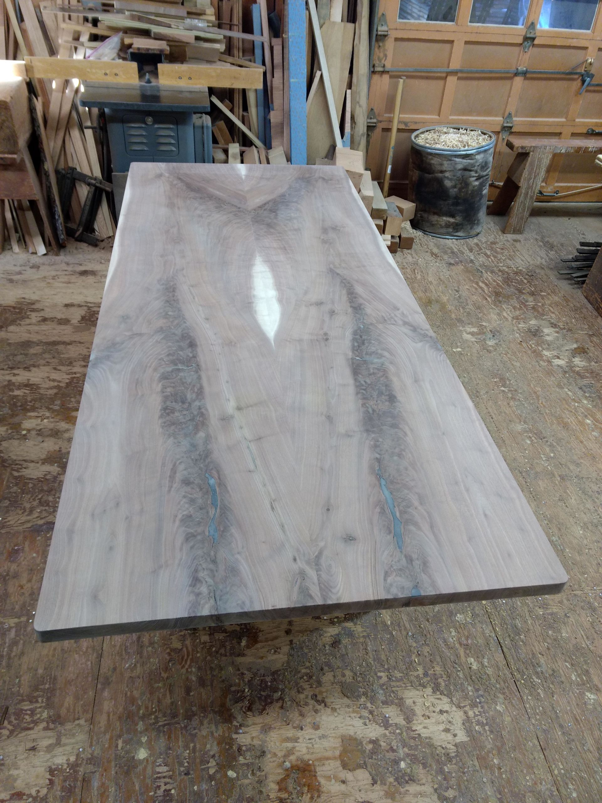 Large, rectangular, unfinished wood table in a workshop, showcasing the wood grain.