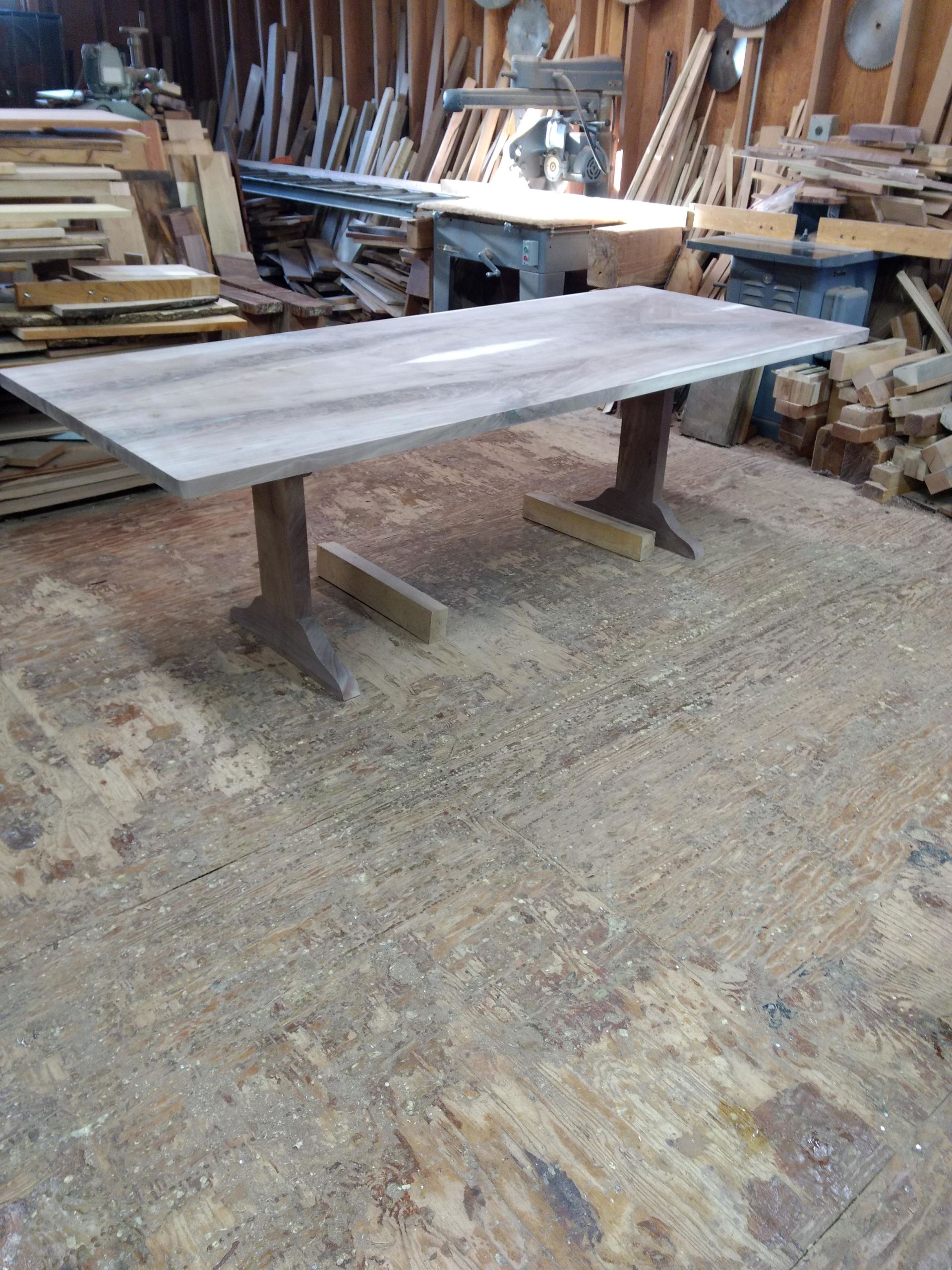 Wooden dining table with pedestal legs in a woodworking shop.