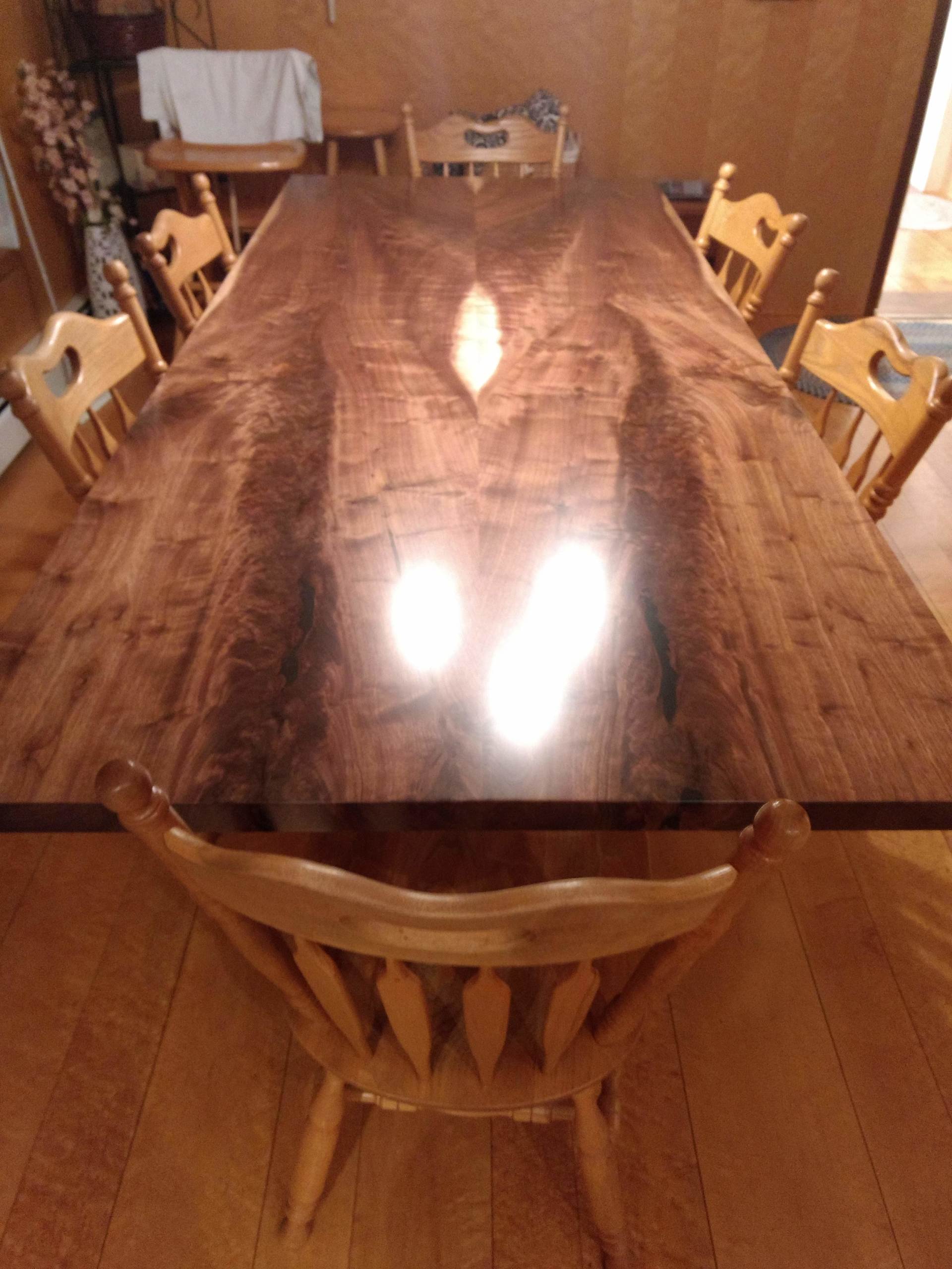 Large wooden dining table with chairs; sunlit, dark wood surface reflects light.