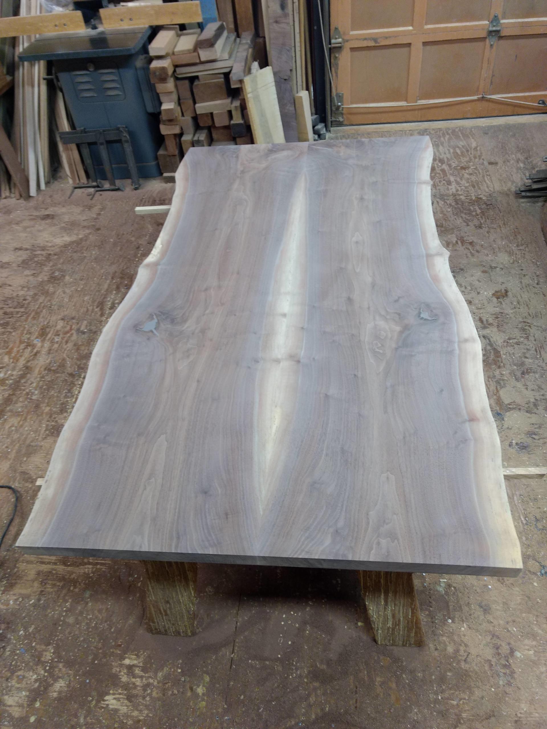 Live edge wood table, grey-brown, on wooden supports in workshop.