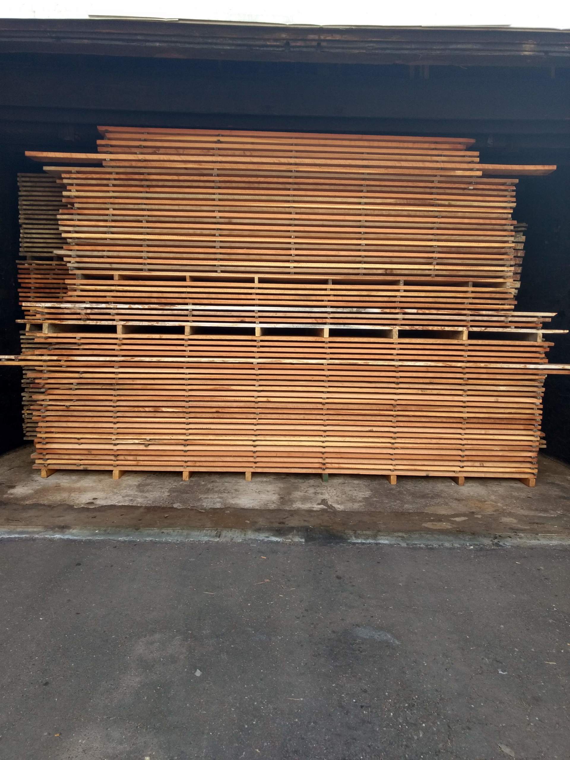 Stacks of wooden boards, varying in size, neatly arranged in a dark storage area.