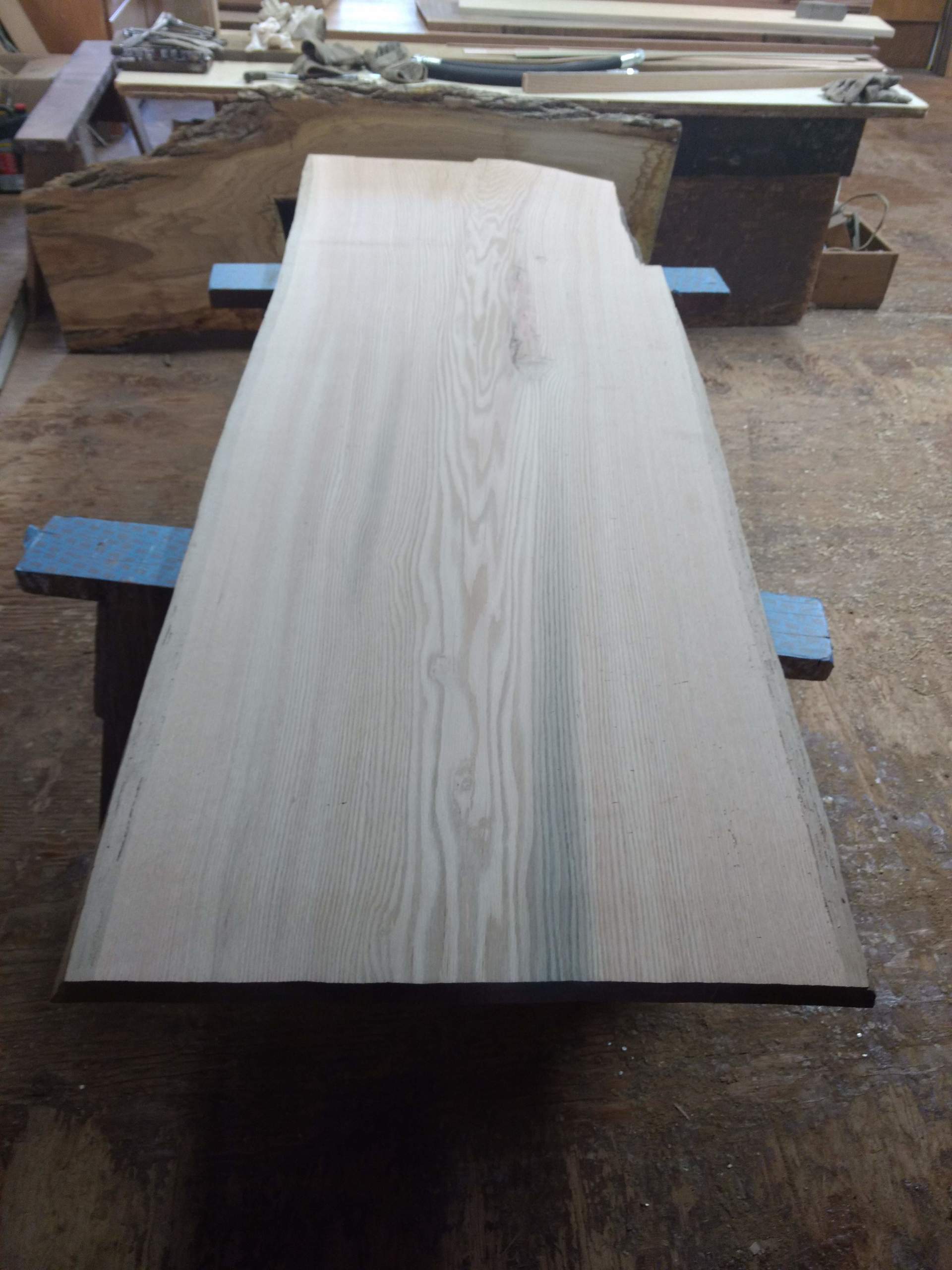 Wooden plank with visible grain rests on blue saw horses in a workshop.