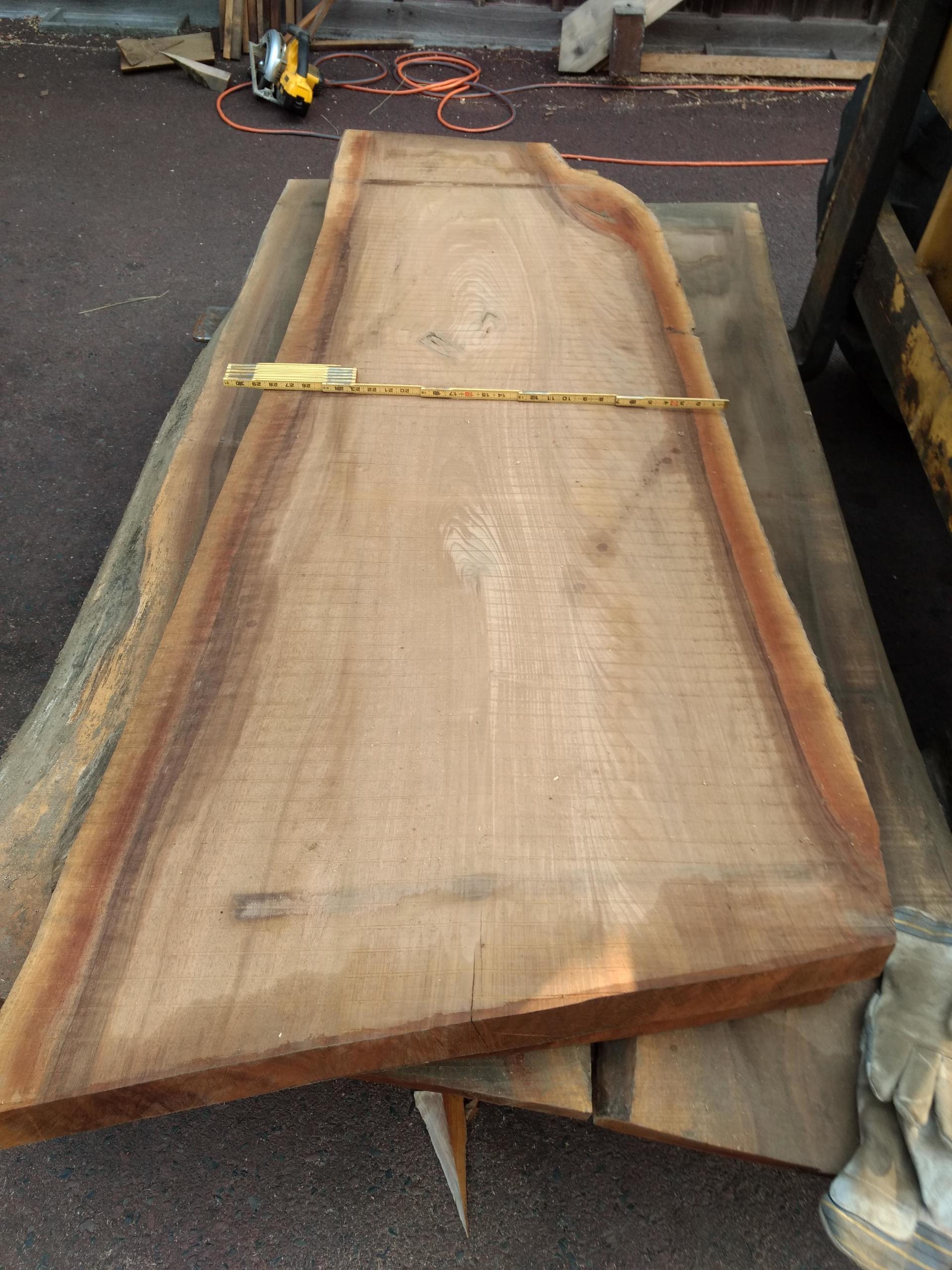 A large, irregular-shaped wooden slab on a wooden platform, a measuring tape across it.