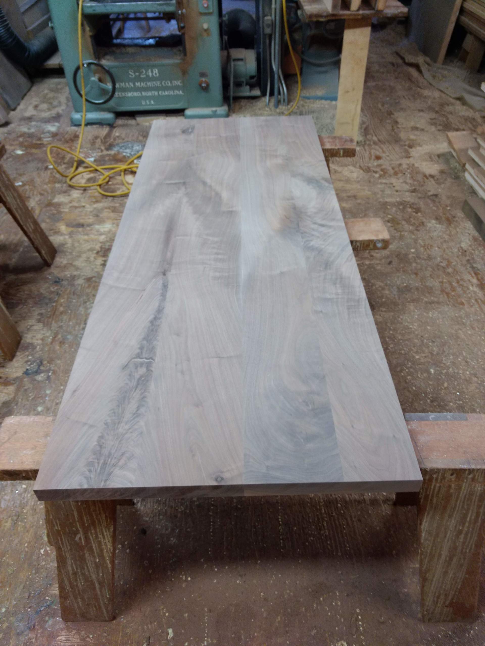 A large, rectangular wooden tabletop resting on two sawhorses, in a workshop setting.
