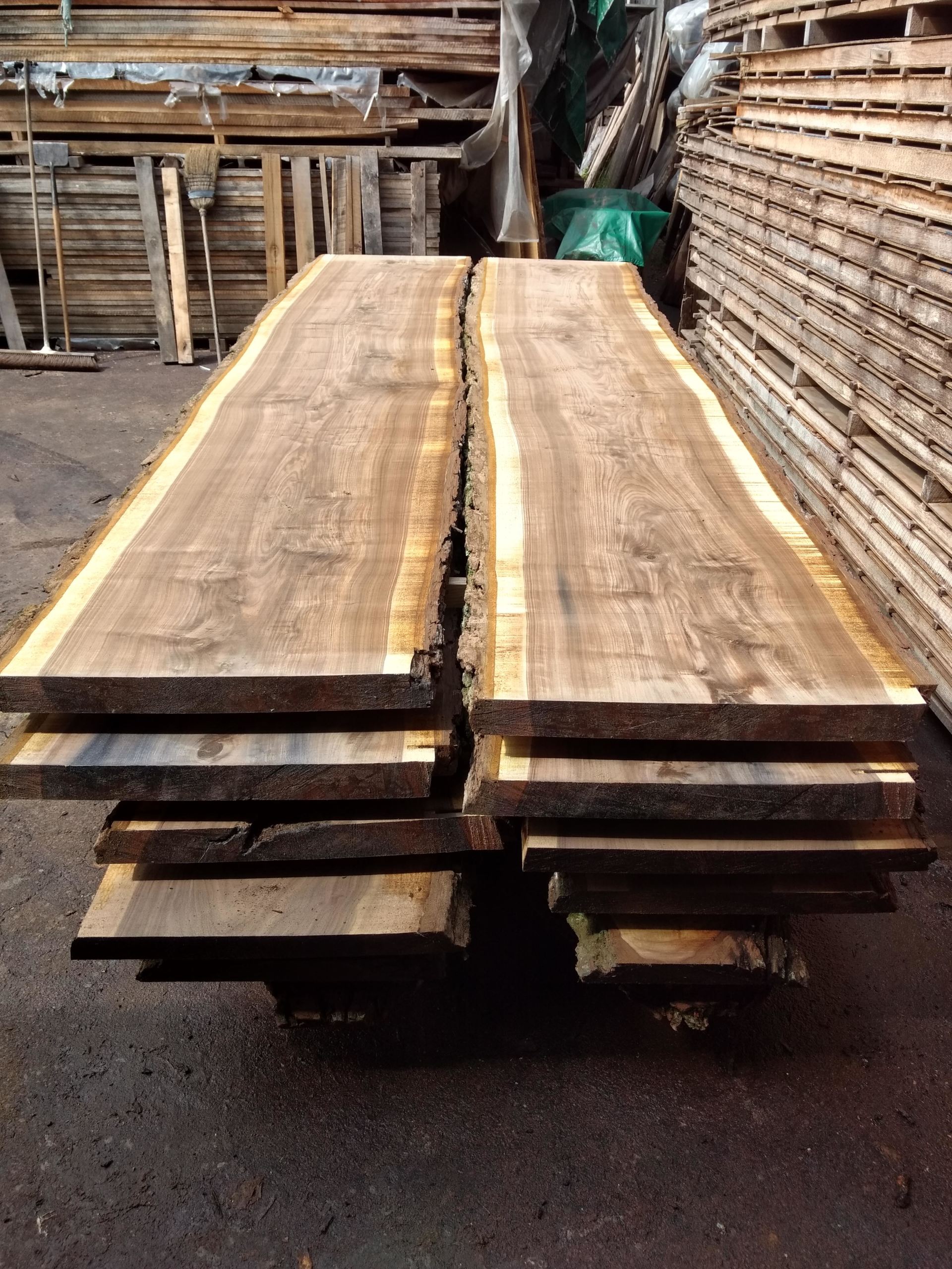Sawn hardwood lumber, stacked. Brown, natural-edged boards in a lumberyard setting.