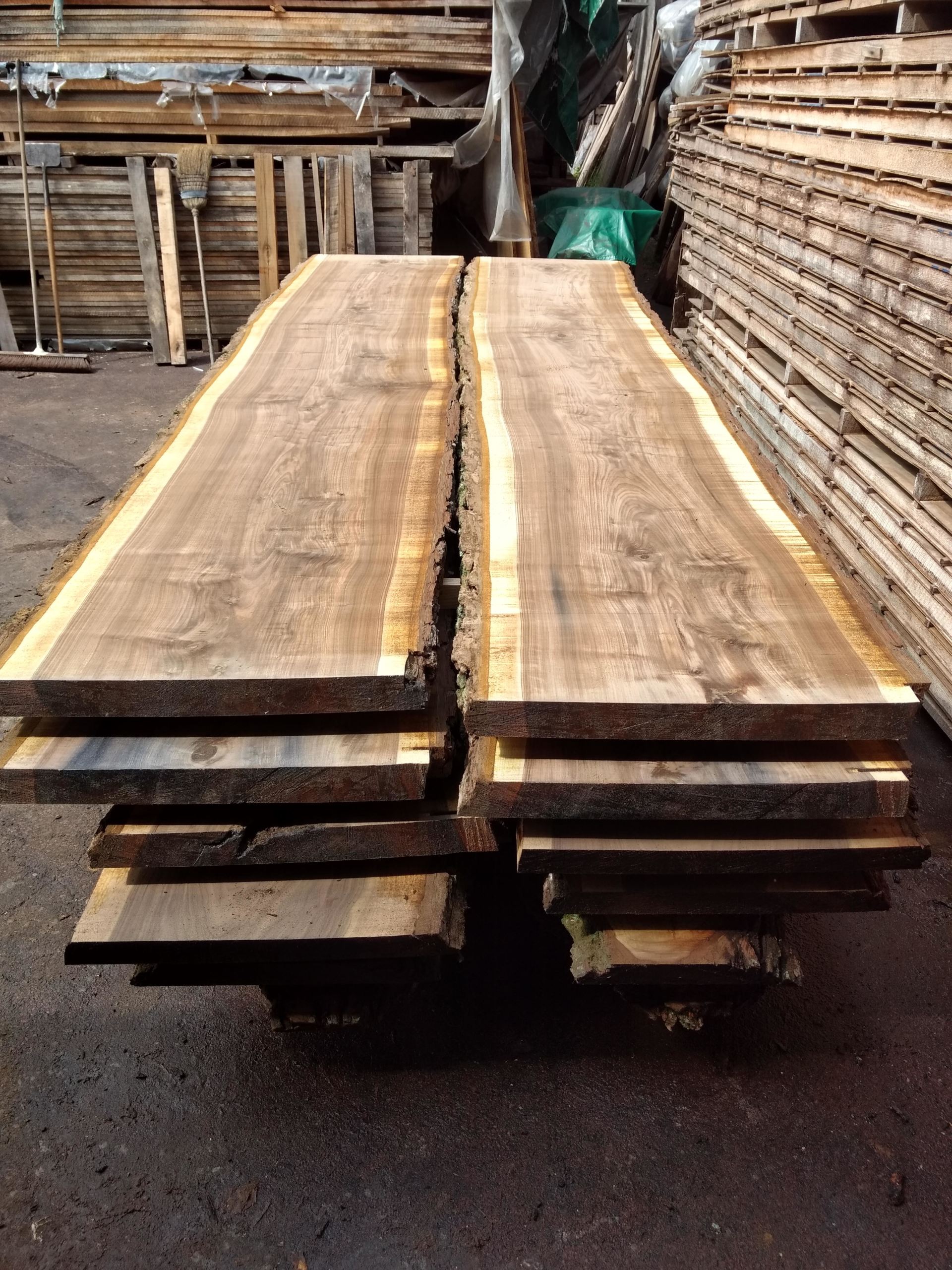 Stack of rough-cut wooden boards with natural edge, in a lumberyard setting.