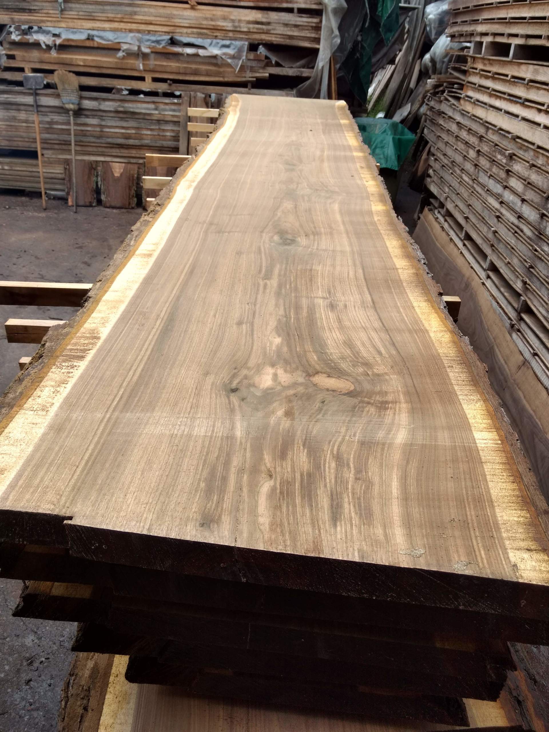 Stack of rough-cut walnut lumber at a lumber yard, showing grain detail and live edge.