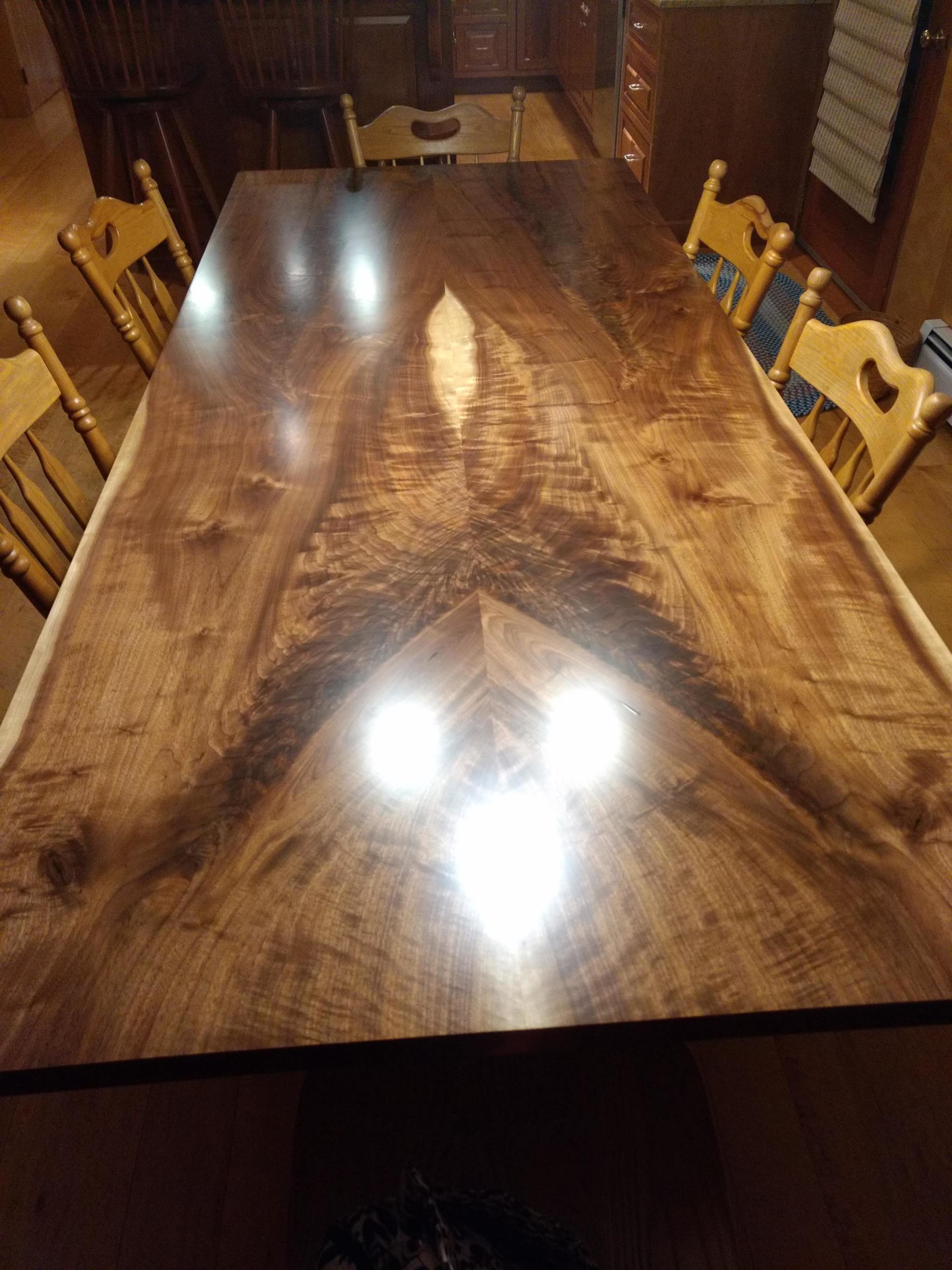 Large wooden dining table with chairs in a dimly lit room, glossy finish reflects light.