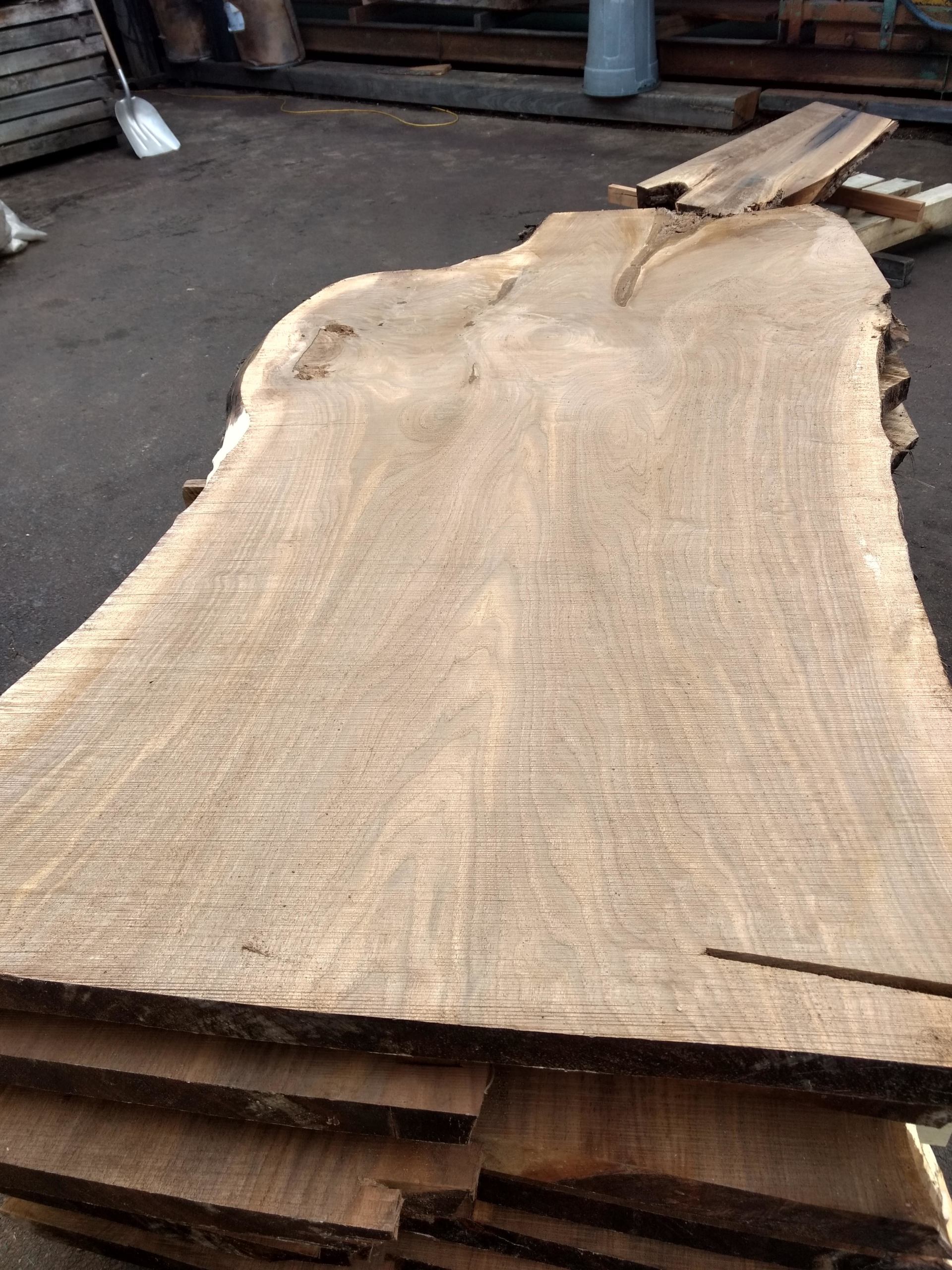Stack of rough-cut, light brown wood planks with irregular edges.