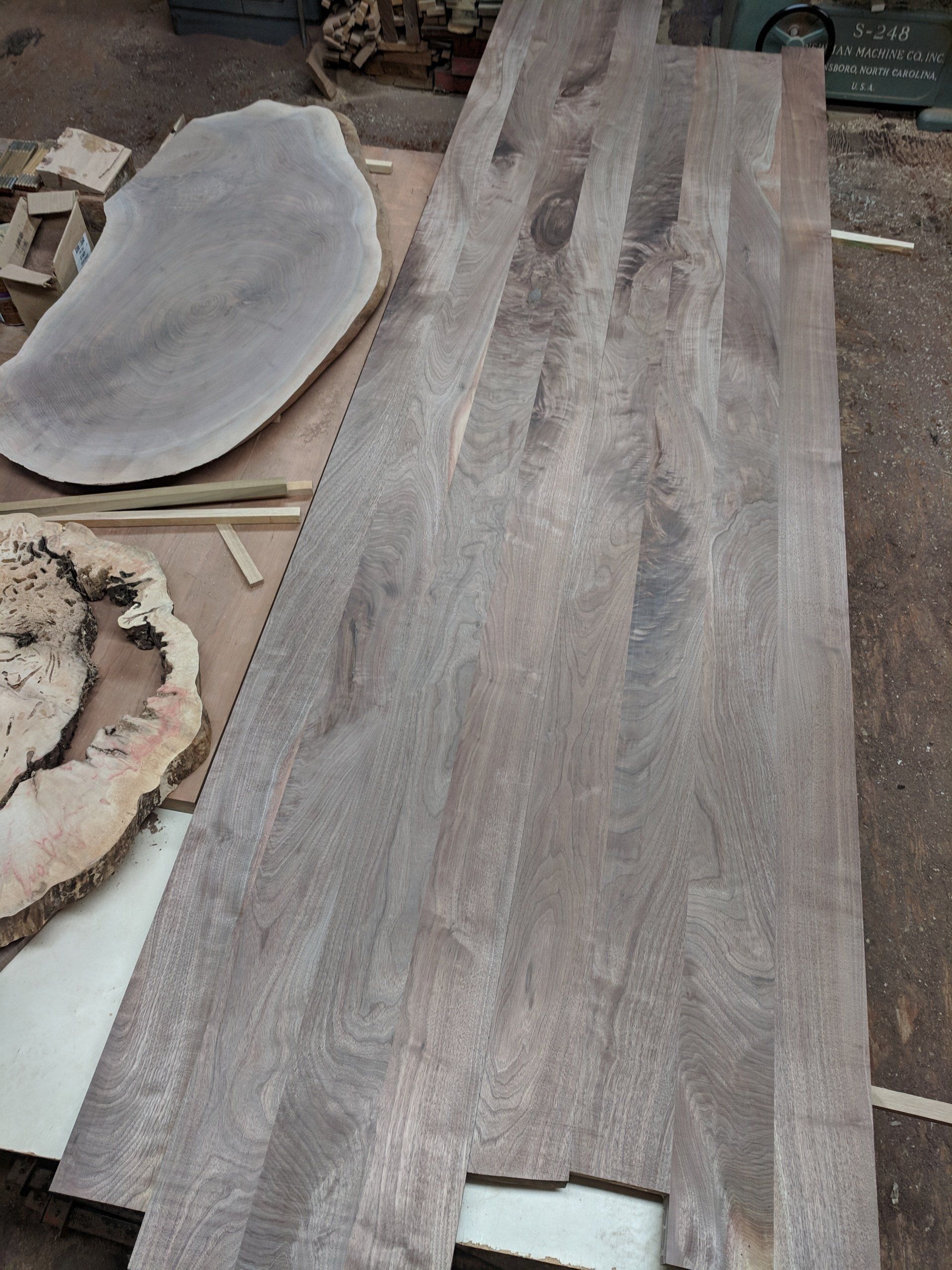 Wooden boards and irregularly shaped slabs on a workshop floor; gray-brown hues.