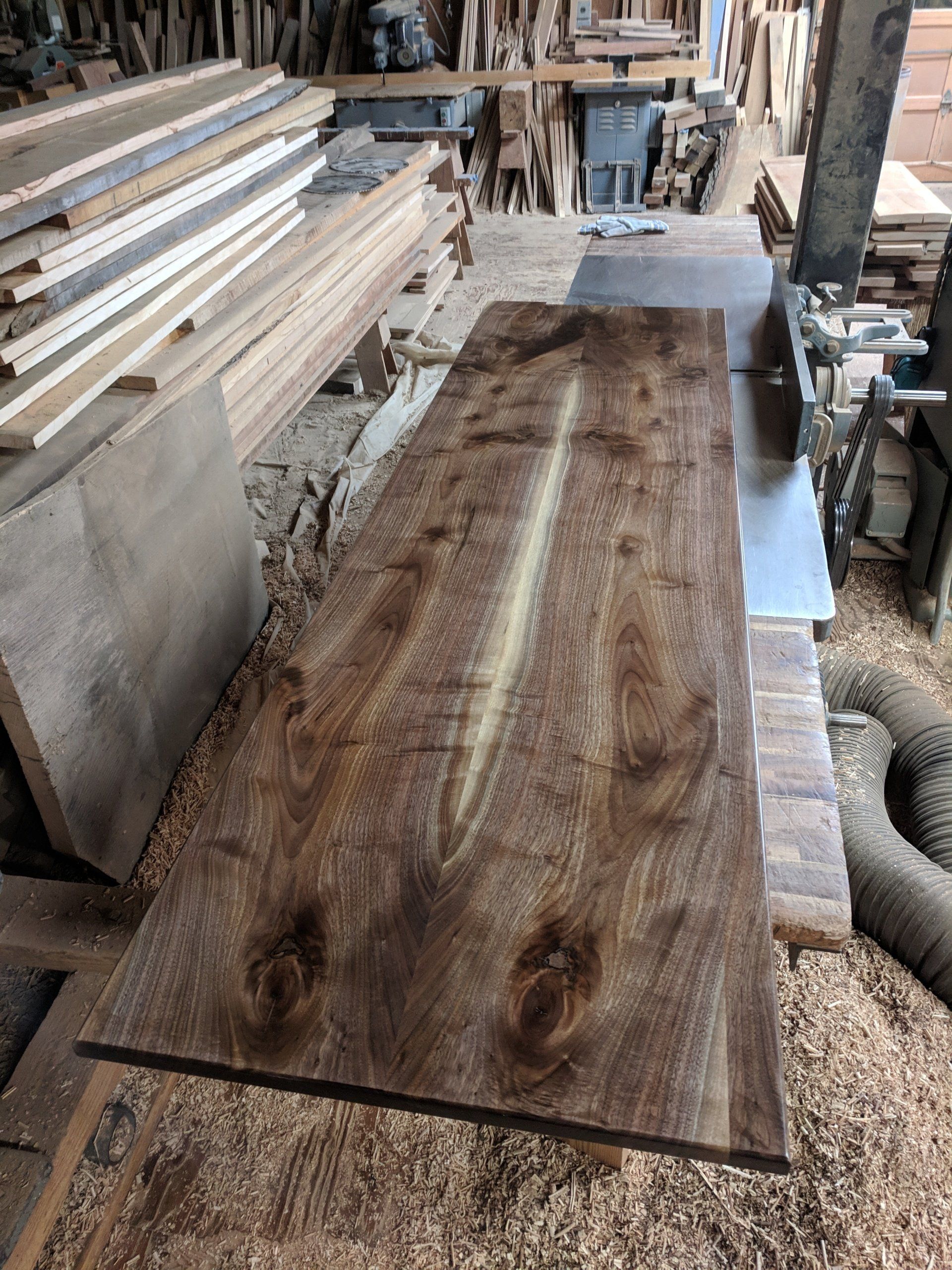 Wood slab with dark, swirling grain, lying on a workbench in a wood shop.
