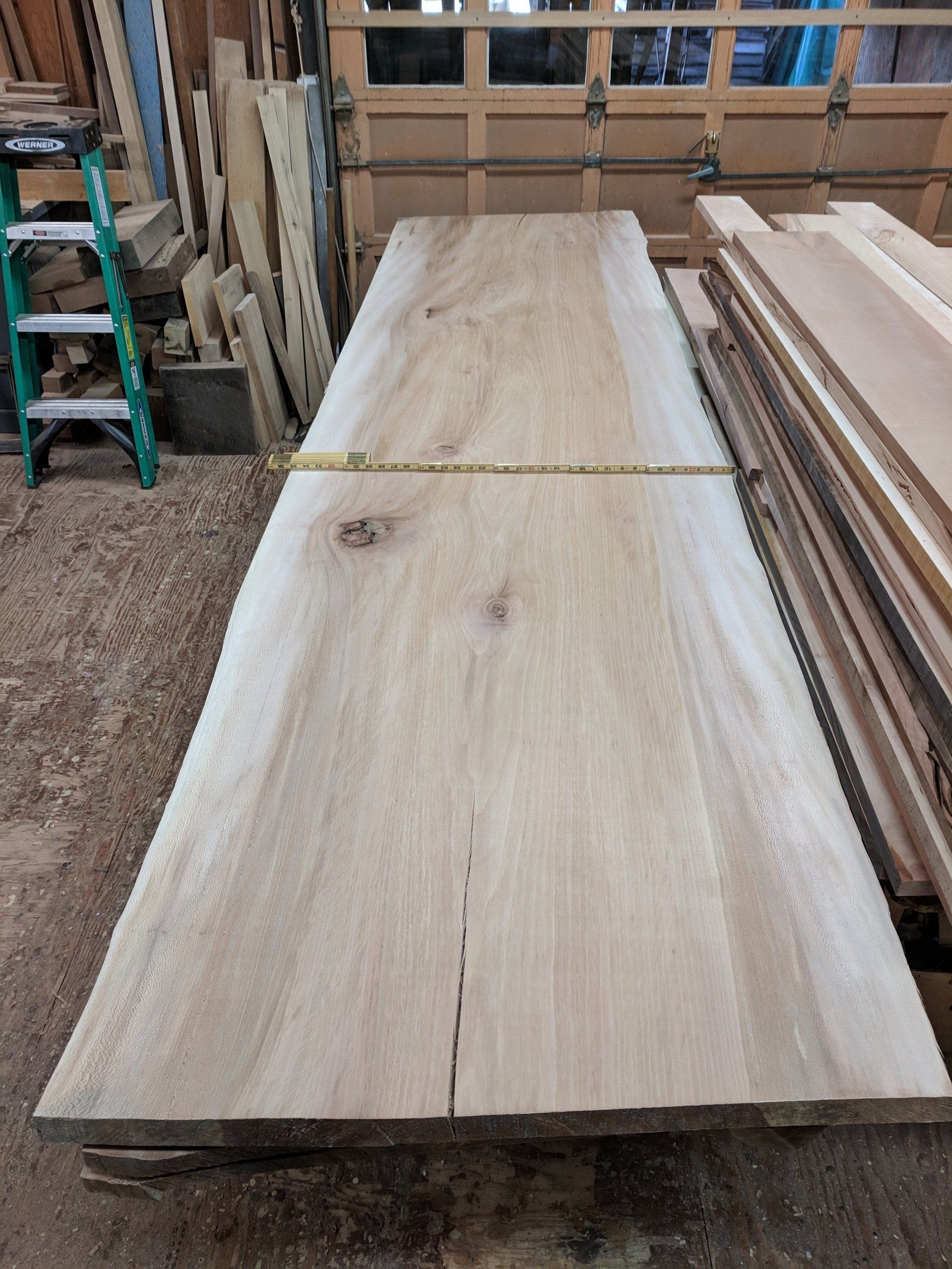 A large, light-colored wooden slab with a crack, lying flat in a workshop.