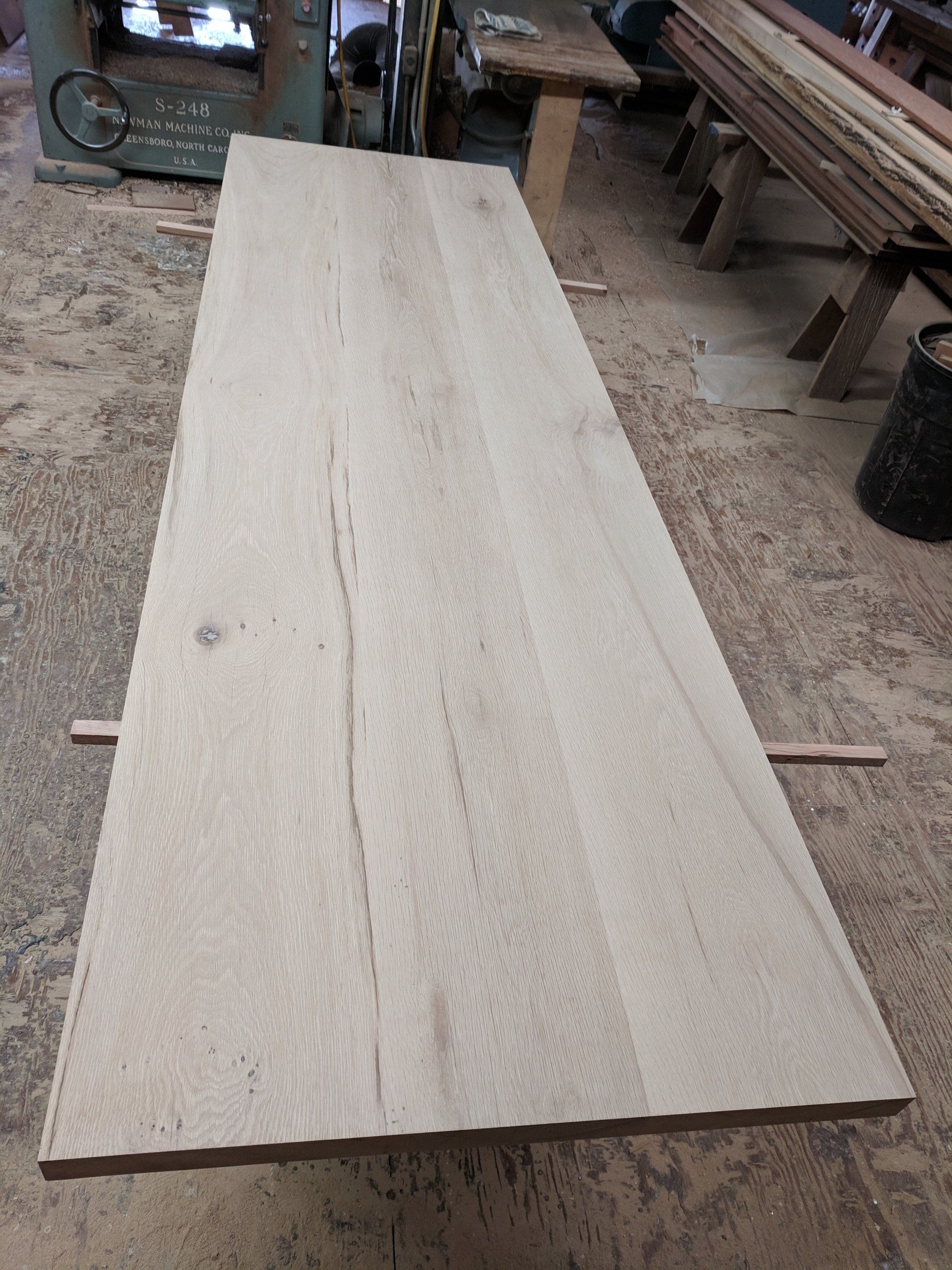 Wooden plank laid flat in a workshop, with visible grain and light brown color.