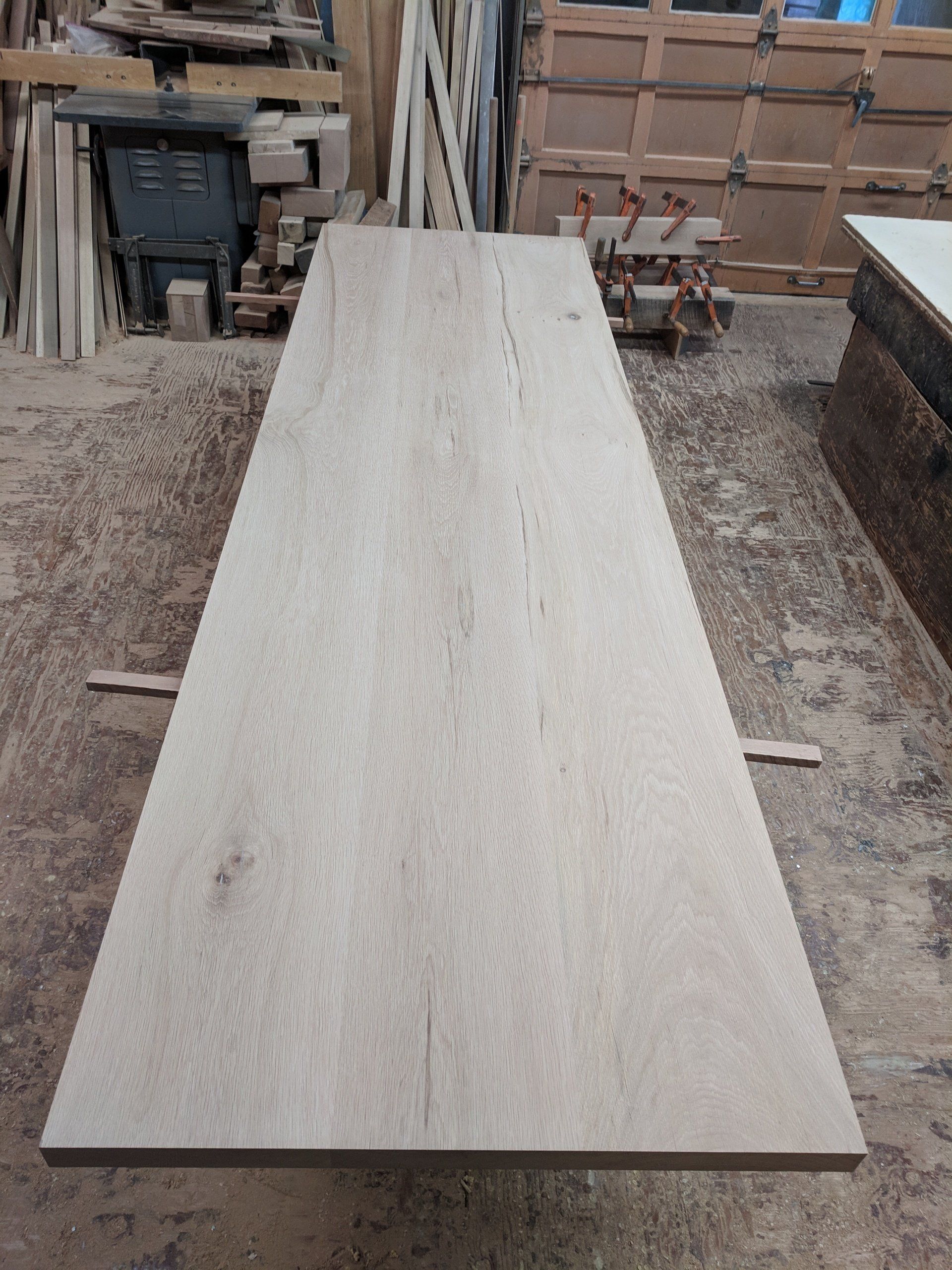 Long, unfinished wooden tabletop in a woodworking shop.